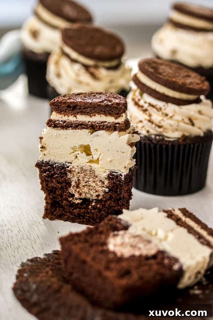 A chocolate cookies and cream cupcake sliced in half, revealing the creamy cookie crumb filling inside.