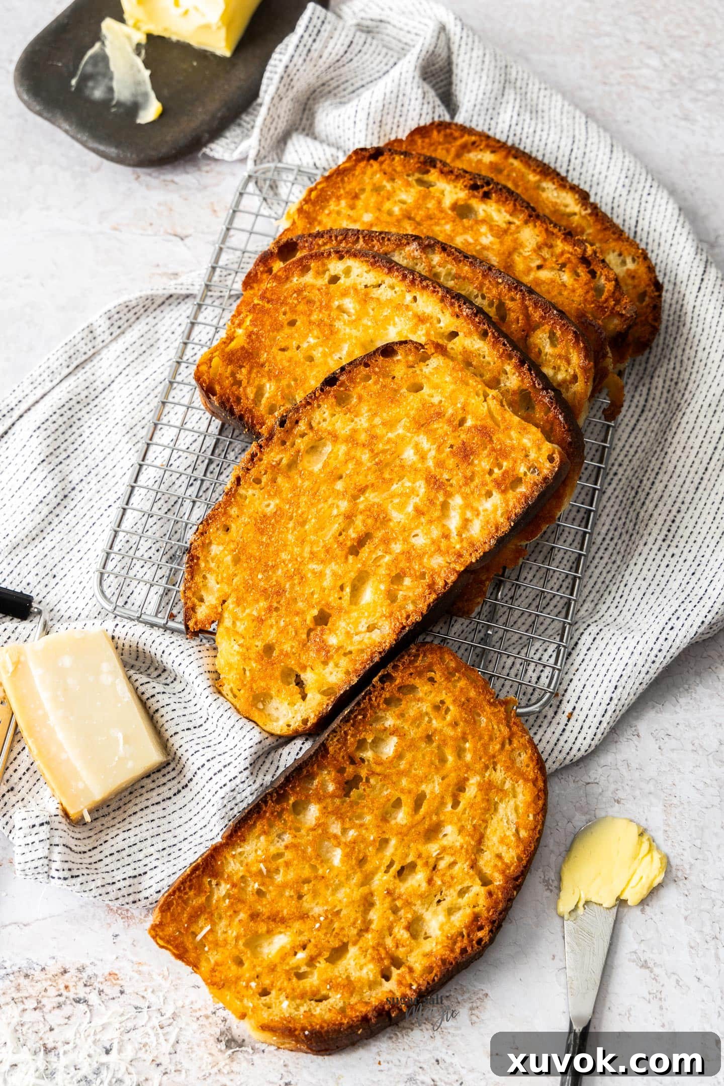 Top down view of a batch of parmesan toast on a wire rack, showcasing its golden-brown crust and cheesy texture.