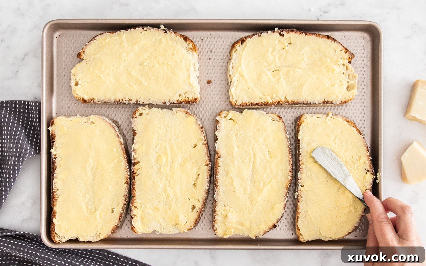 A hand spreading parmesan butter evenly on one side of a slice of bread.