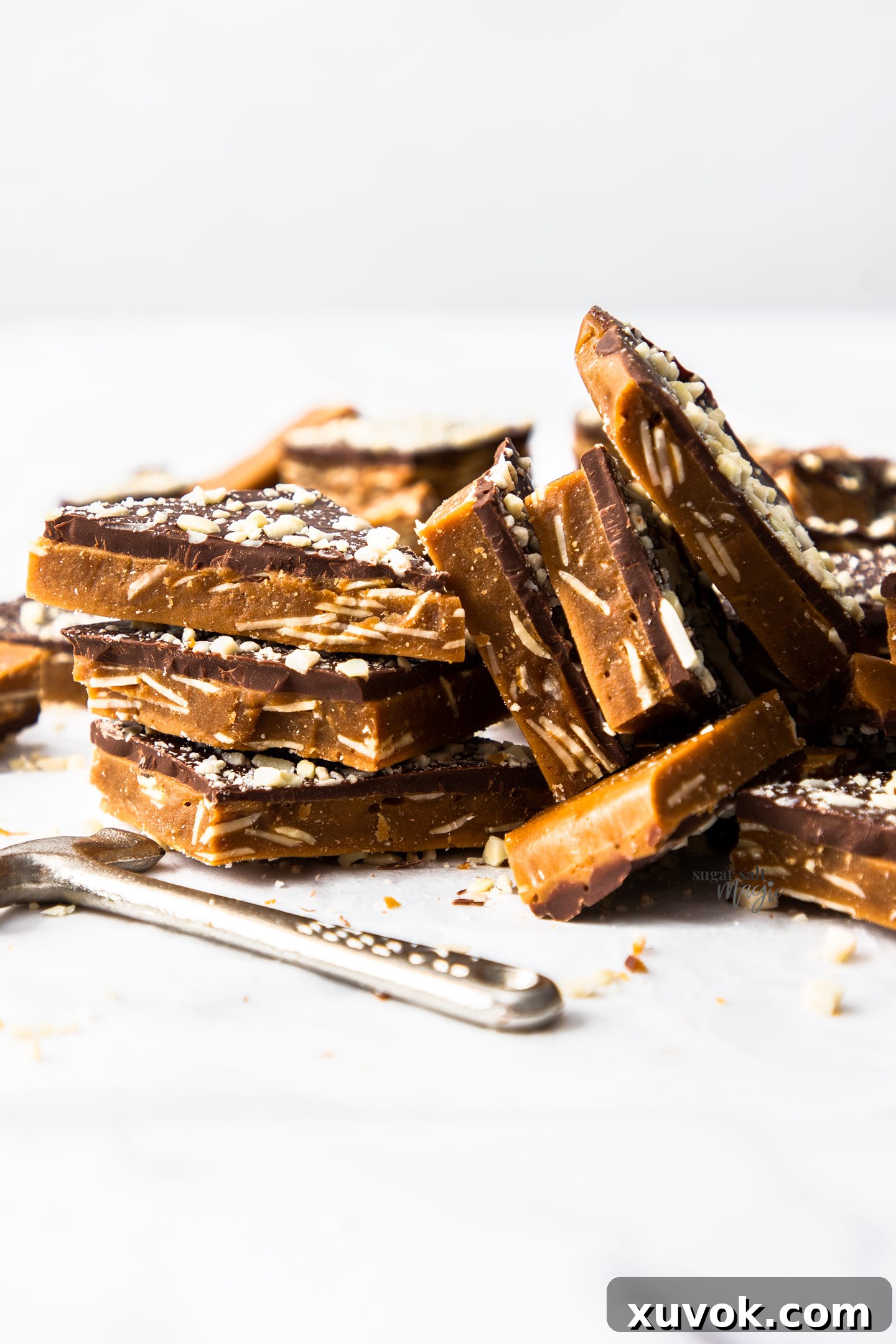 A beautifully arranged stack of golden almond buttercrunch toffee pieces, glistening with chocolate and nuts.