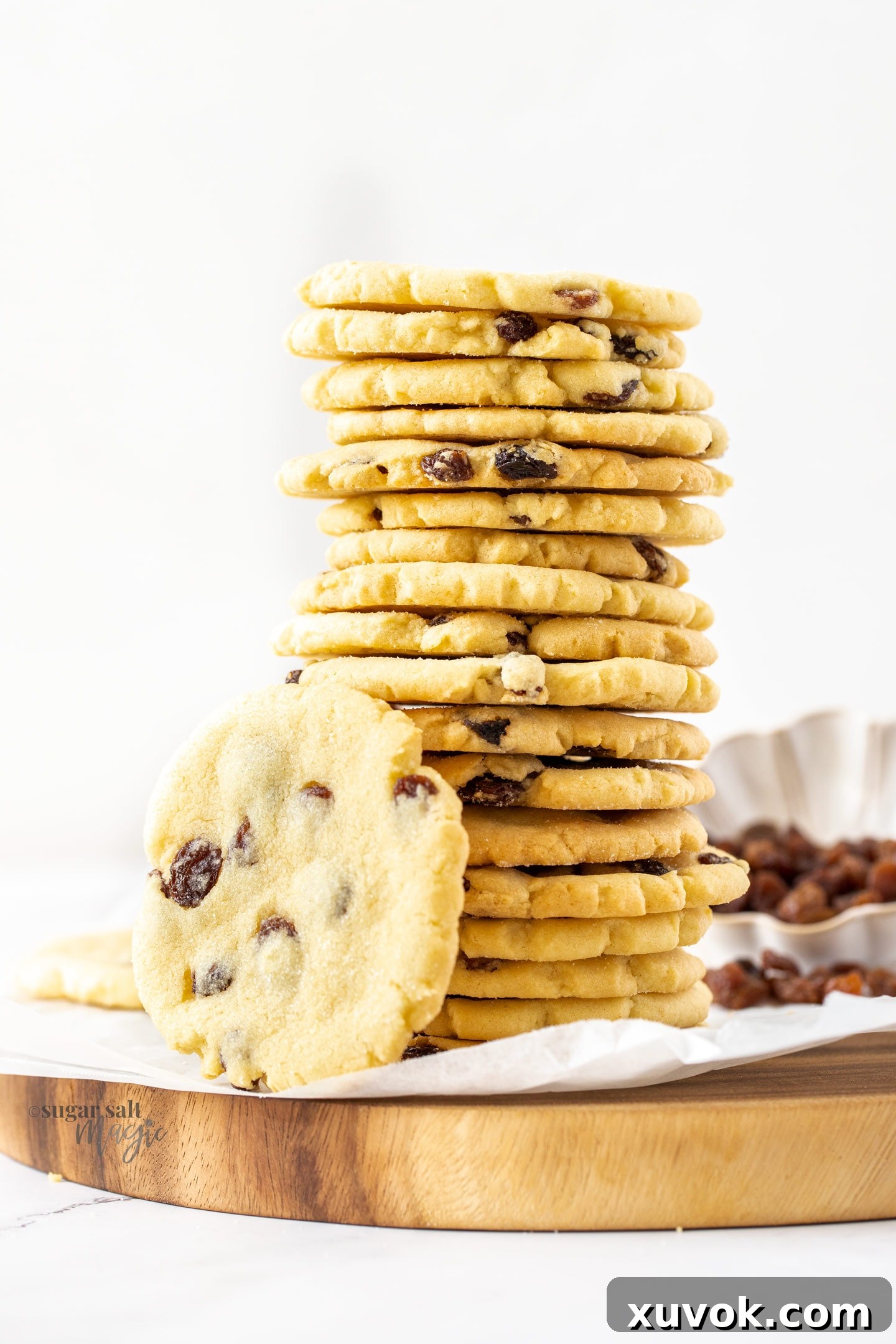 A very tall stack of golden buttery sultana cookies on a wooden board, highlighting their inviting texture and generous sultana content.