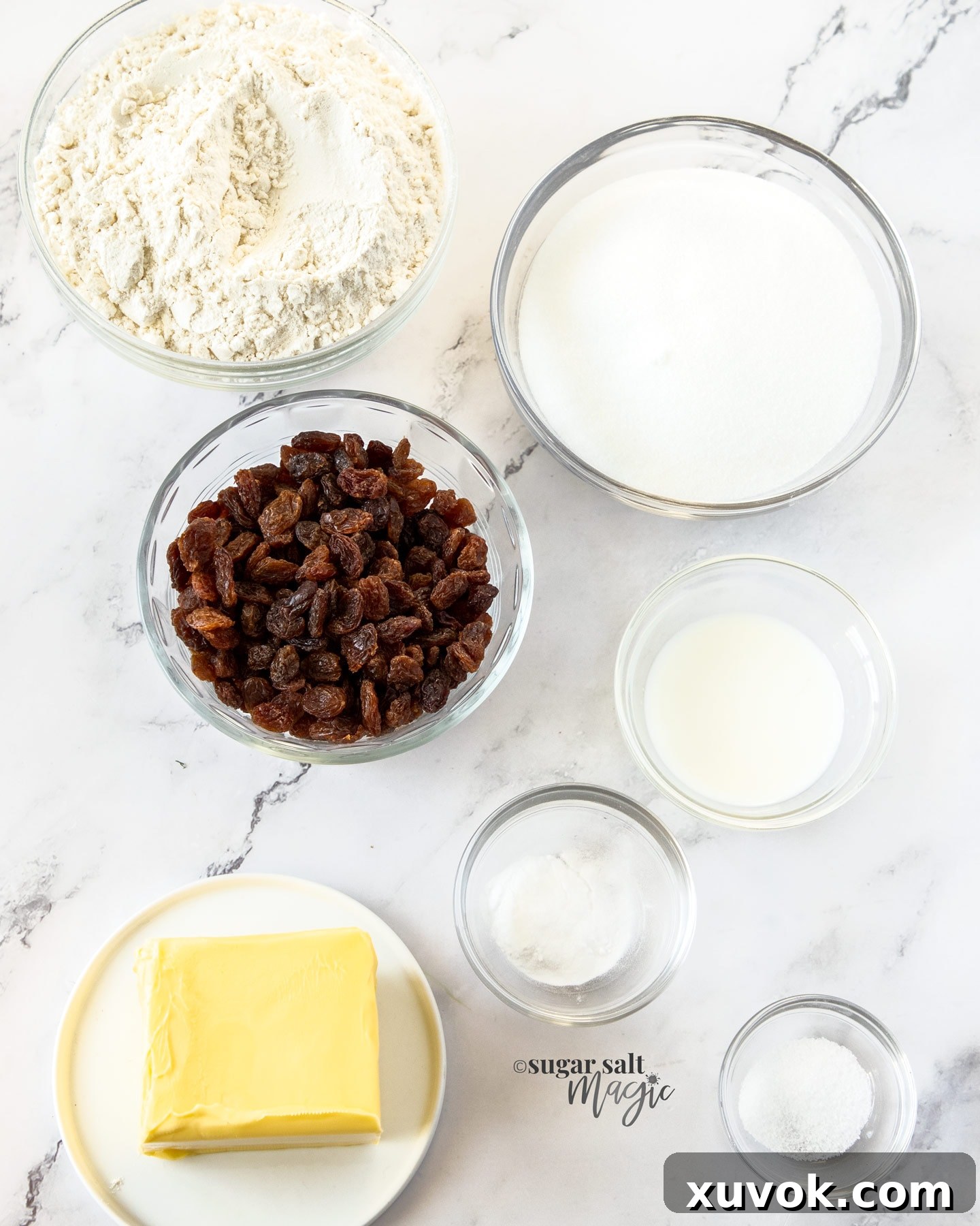 Ingredients for sultana cookies in glass bowls on a marble benchtop, neatly arranged for baking.