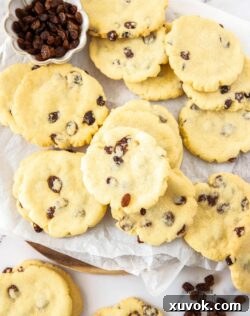 A pile of sultana filled cookies with a small bowl of sultanas.