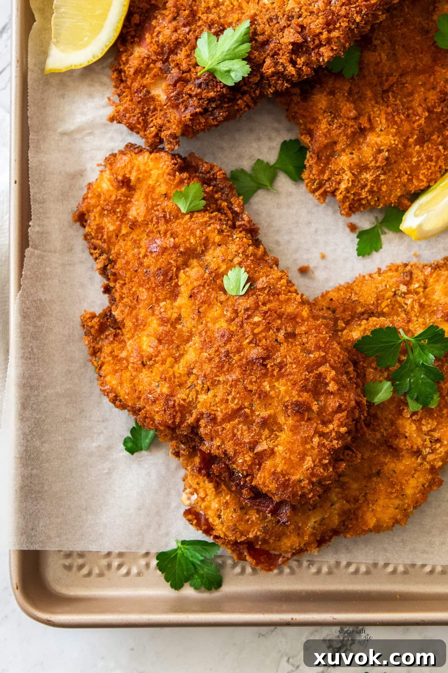 Closeup top down view of golden, crispy homemade chicken schnitzel garnished with fresh parsley and a lemon wedge, ready to be served.