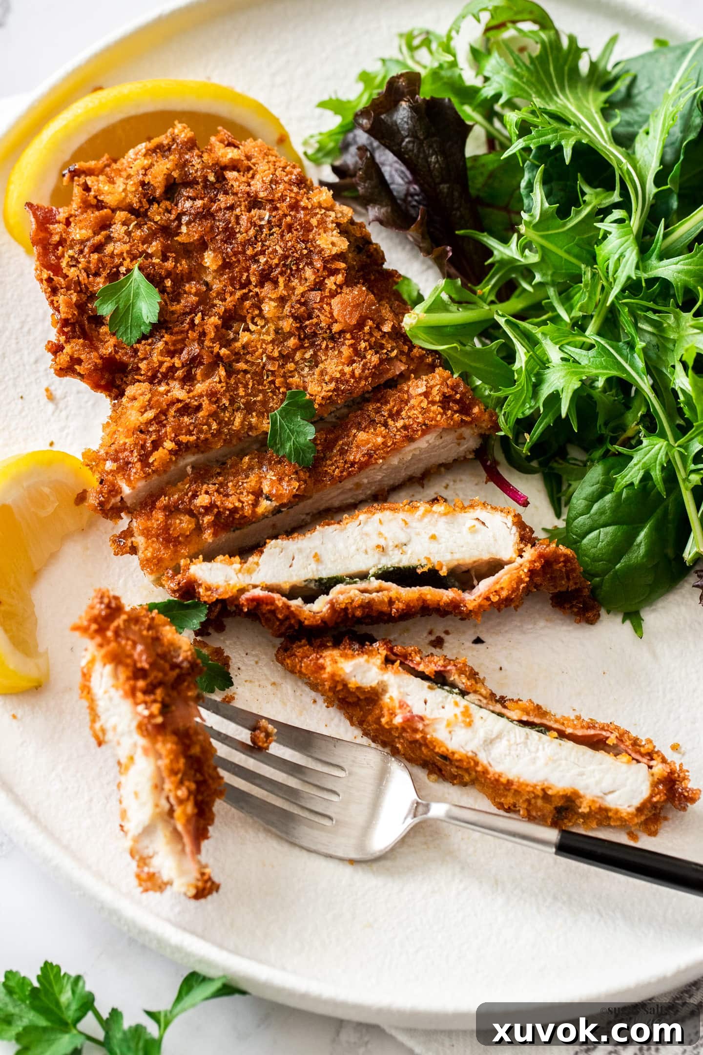 A perfectly cooked Saltimbocca chicken schnitzel served on a white plate with a fresh green salad and a lemon wedge.