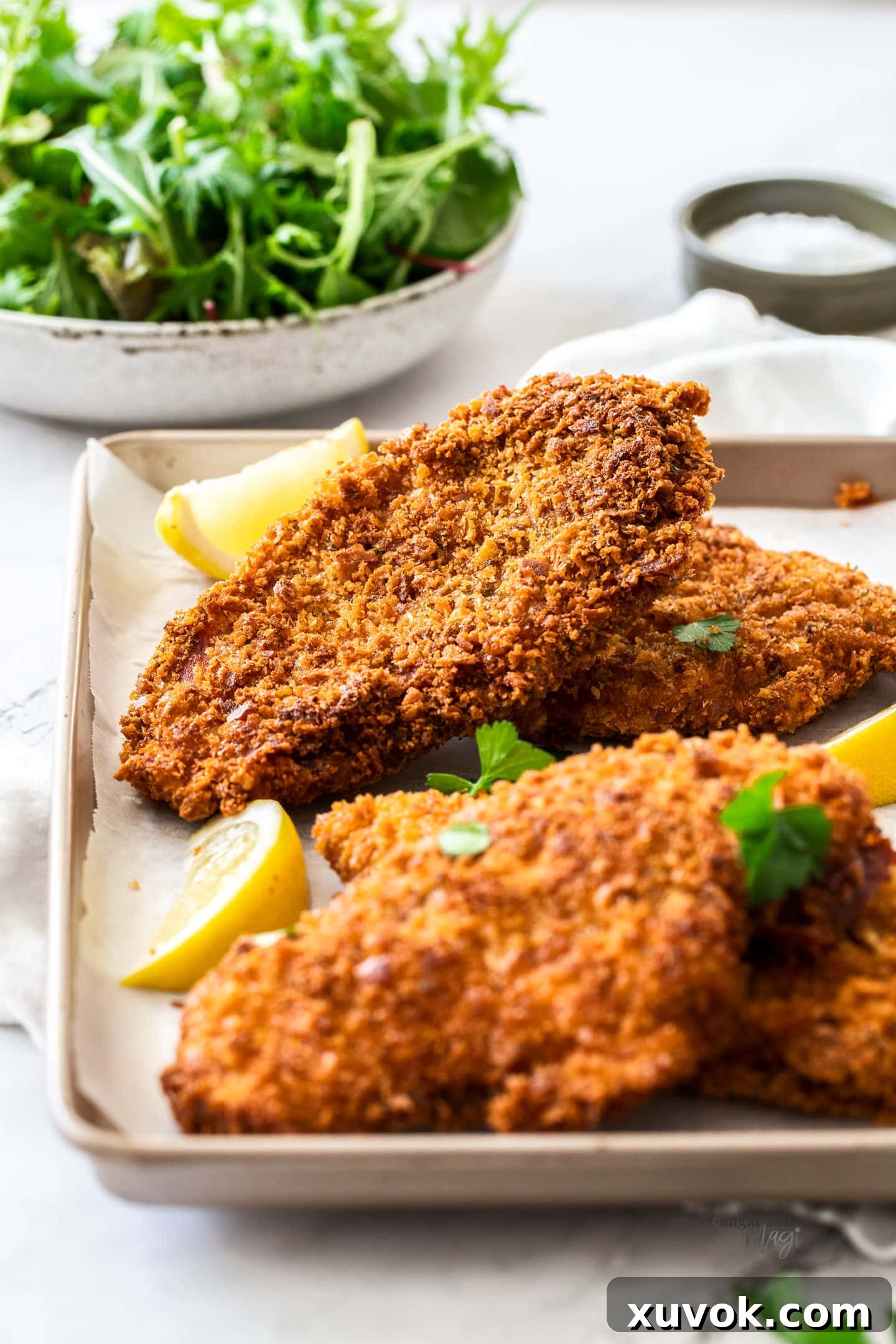 Four crunchy golden brown chicken schnitzels arranged on a baking tray with fresh lemon wedges, ready to serve.