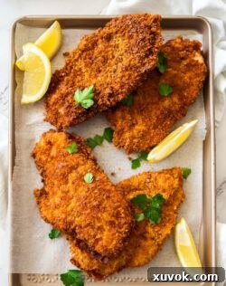 4 crunchy golden brown schnitzels on a baking tray with lemon wedges.