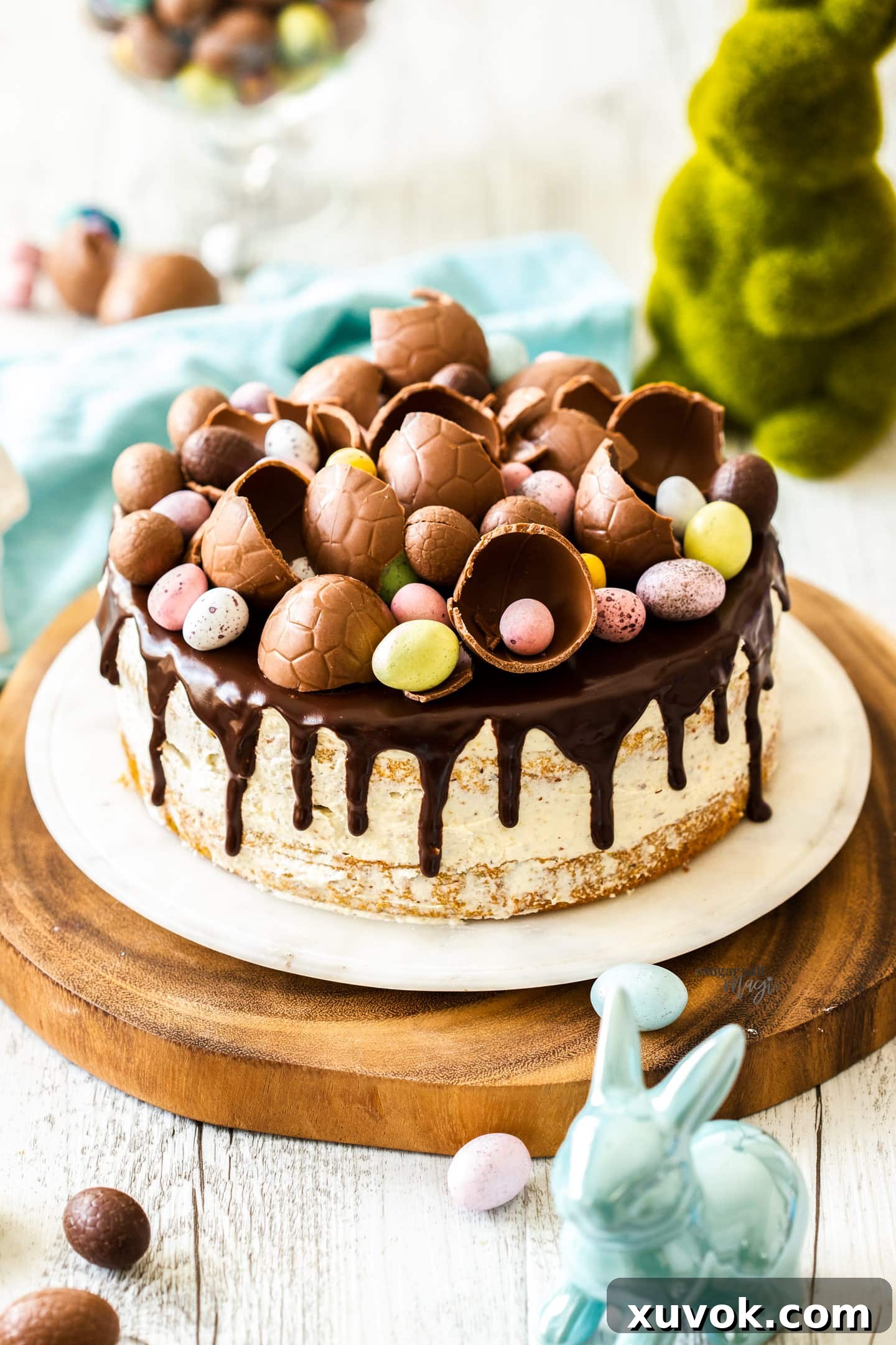 A whole hazelnut cake, generously topped with chocolate ganache and an array of vibrant Easter eggs, presented on an elegant cake platter, ready for celebration.