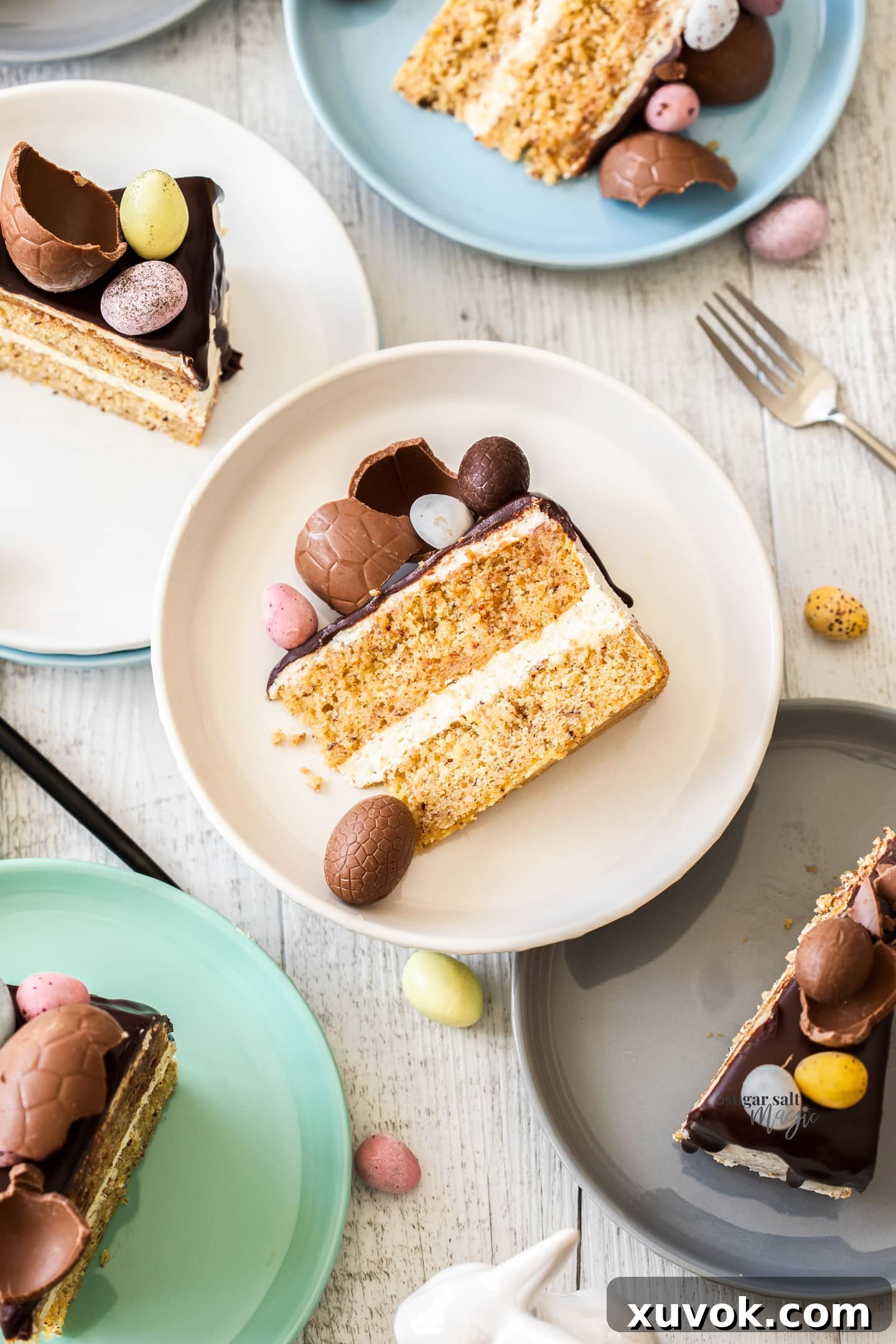 Individual slices of hazelnut cake, each topped with a delicate Easter egg, artfully arranged on colorful dessert plates.