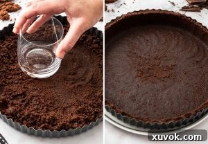 A hand using a glass to press cookie crumbs into a tart pan.