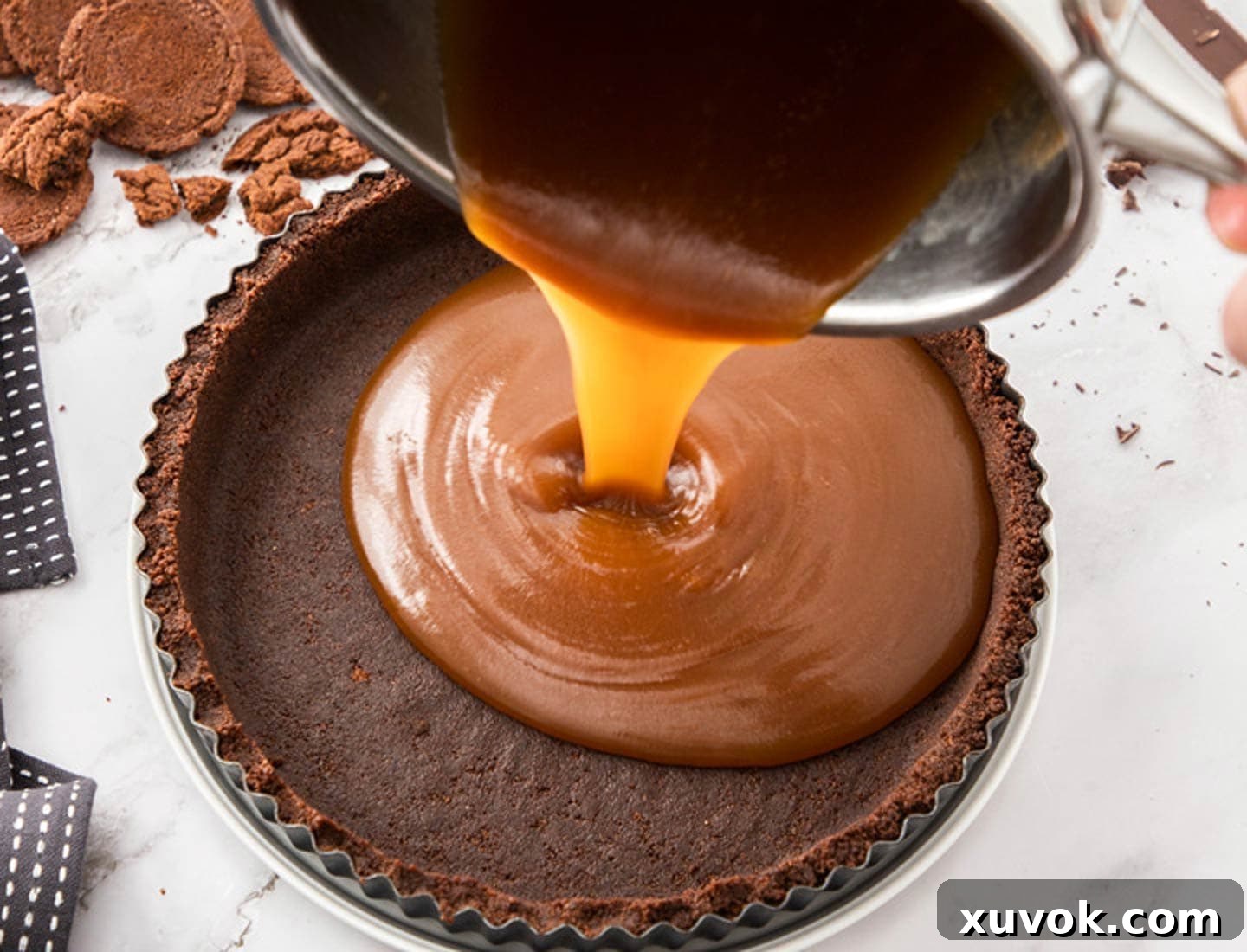 Caramel being poured into a chocolate cookie tart shell.