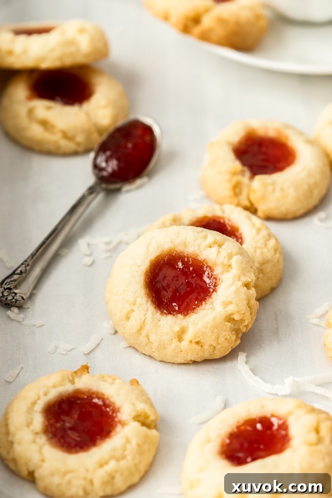 Seven perfectly baked Coconut Jam Drops arranged on a white background, with a spoonful of glistening strawberry jam beside them.