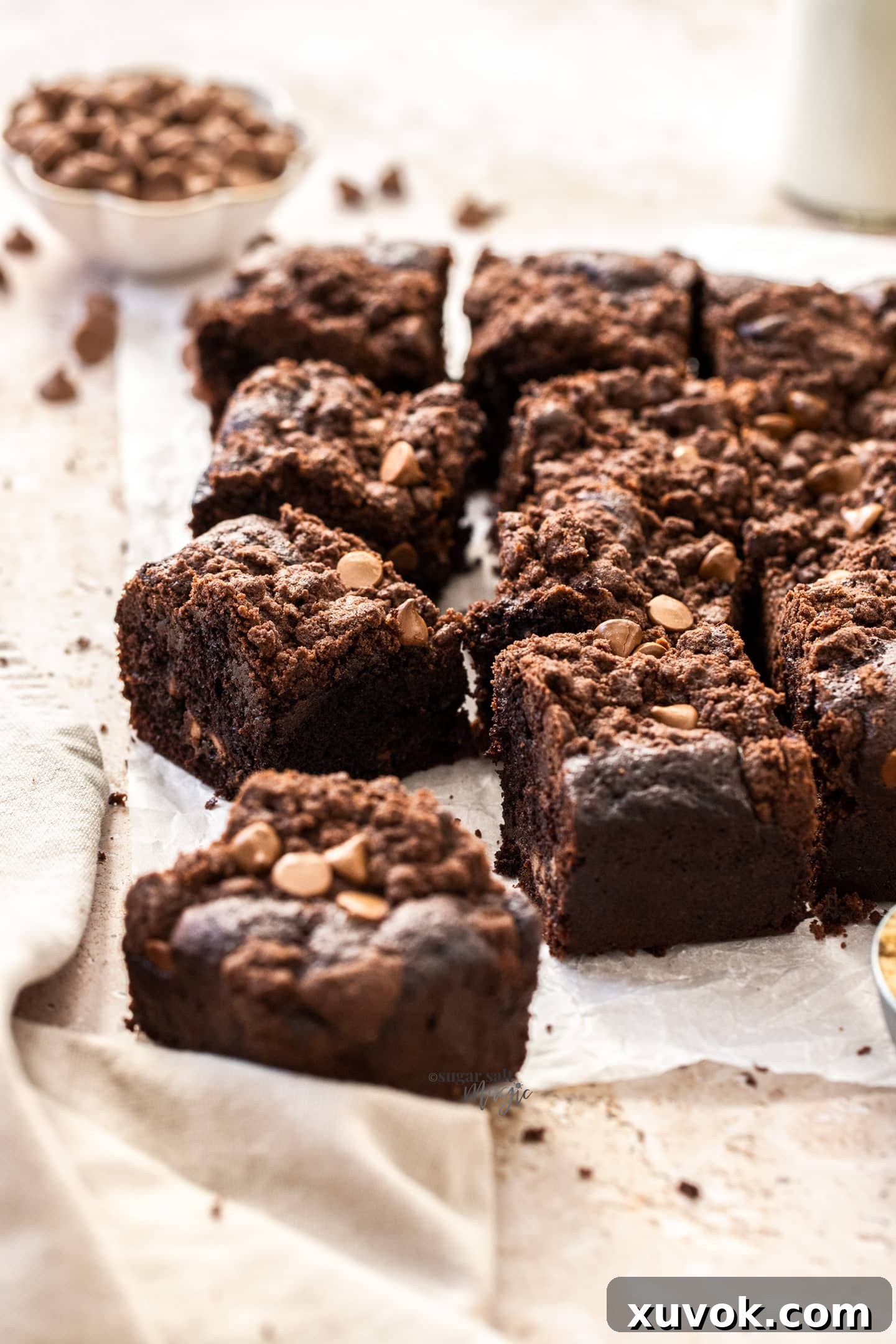 A batch of chocolate crumb cake slices on a sheet of baking paper with choc chips behind. Each slice reveals layers of moist chocolate cake and crunchy streusel.