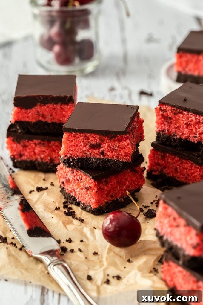 Stacks of cherry ripe slice on brown parchment paper, with a knife in front and a glass of cherries as the back