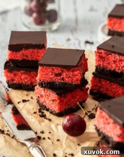 Stacks of cherry ripe slice on brown parchment paper, with a knife in front and a glass of cherries as the back
