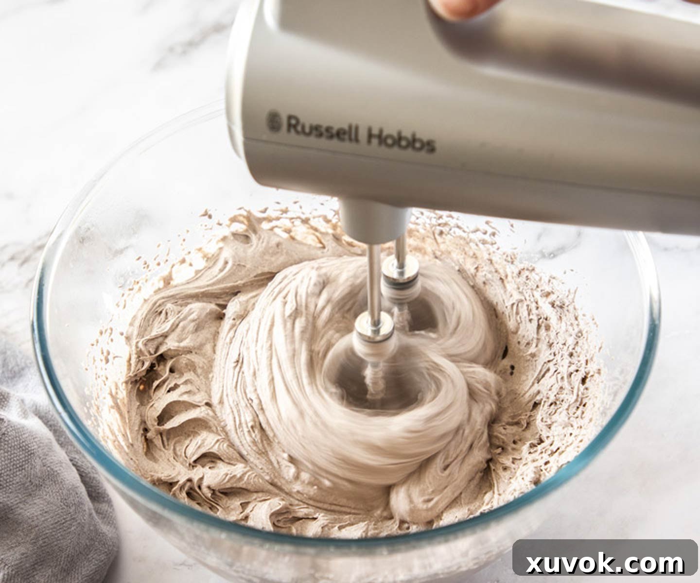 An electric hand beater actively whipping the Oreo and cream mixture in a bowl, creating a visibly lighter, fluffier texture with cookie specks. The motion captures the rapid transformation into a delicious mousse.