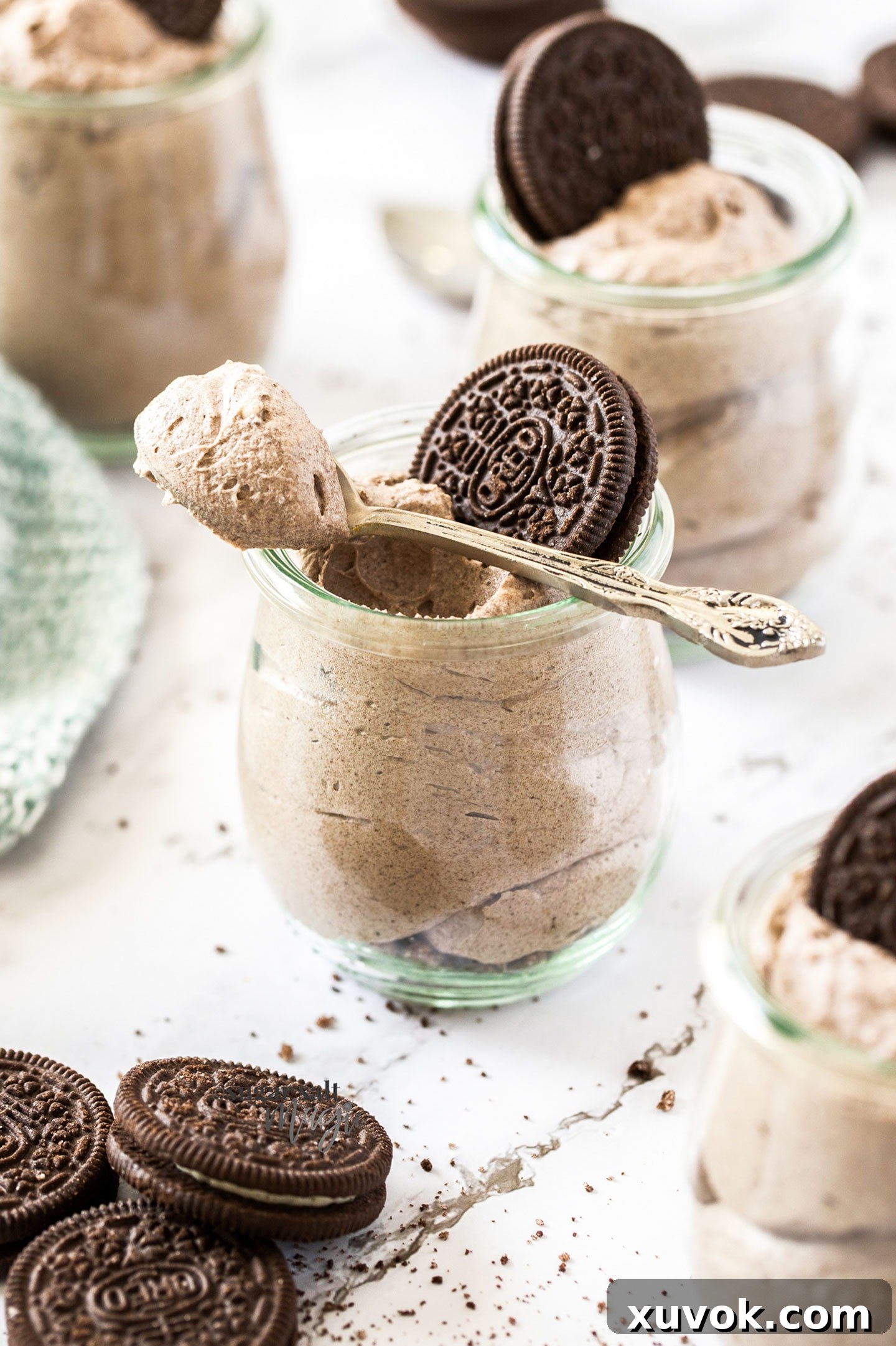 A single, beautifully presented glass jar filled with fluffy Oreo mousse, garnished with a whole Oreo cookie resting on top. A metallic spoon is casually placed across the rim of the jar, ready for tasting. The dessert exudes elegance and homemade comfort.