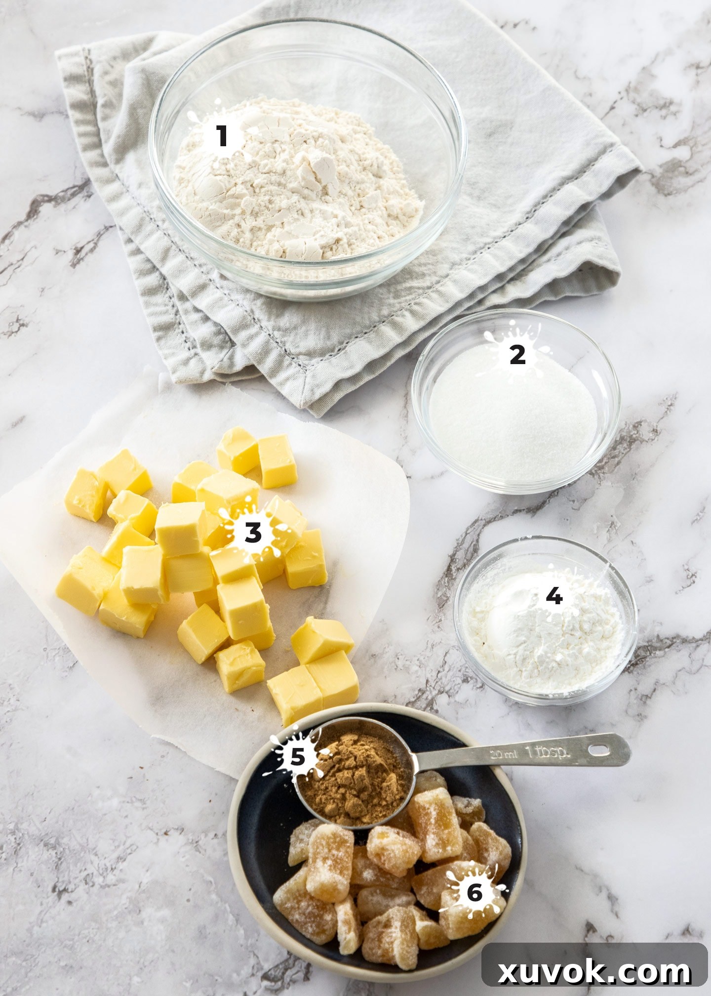 Various ingredients for ginger shortbread laid out on a wooden surface, including butter, flour, sugar, and both ground and candied ginger.