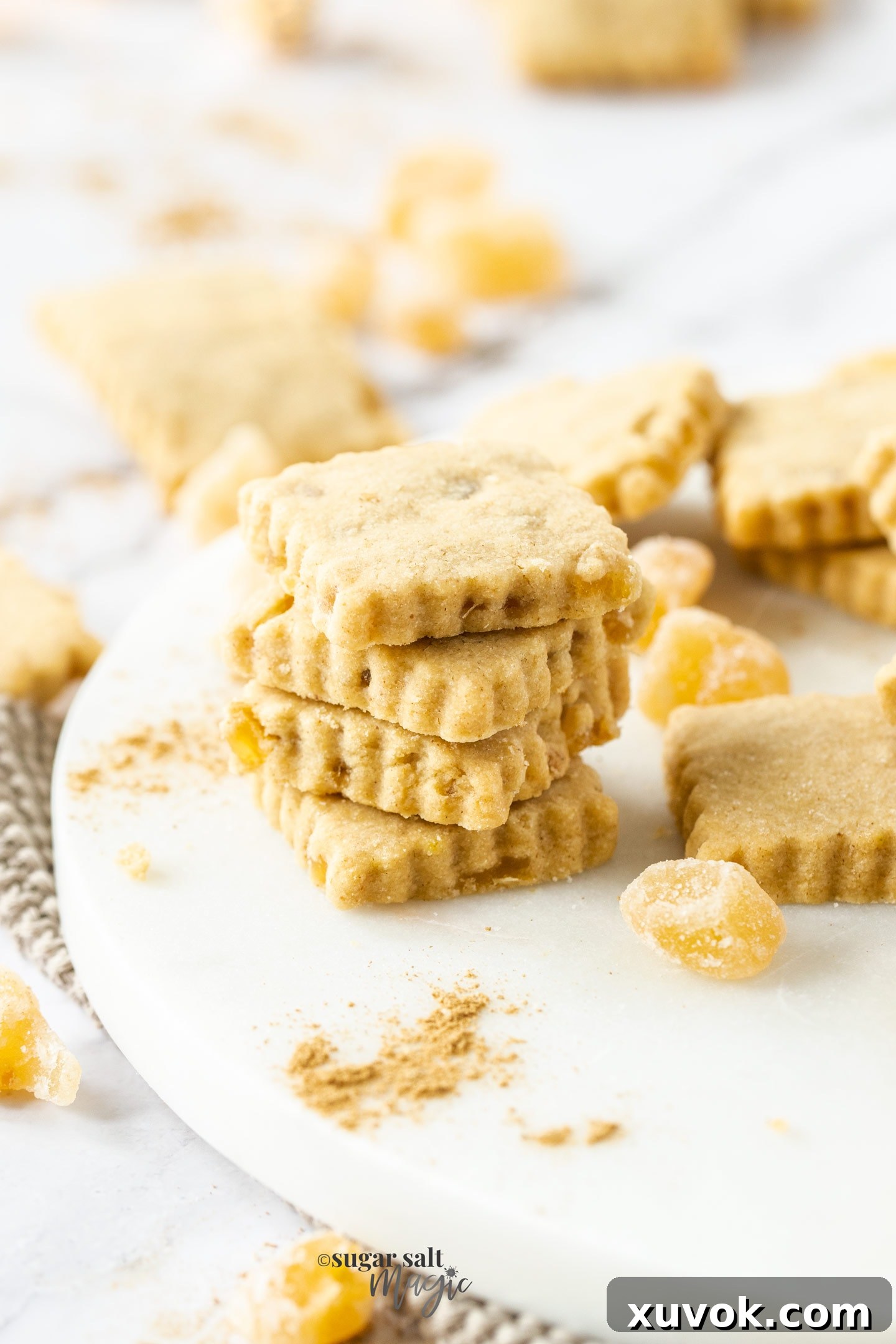 A batch of freshly baked ginger shortbread cookies arranged on a cooling rack, with scattered pieces of candied ginger.