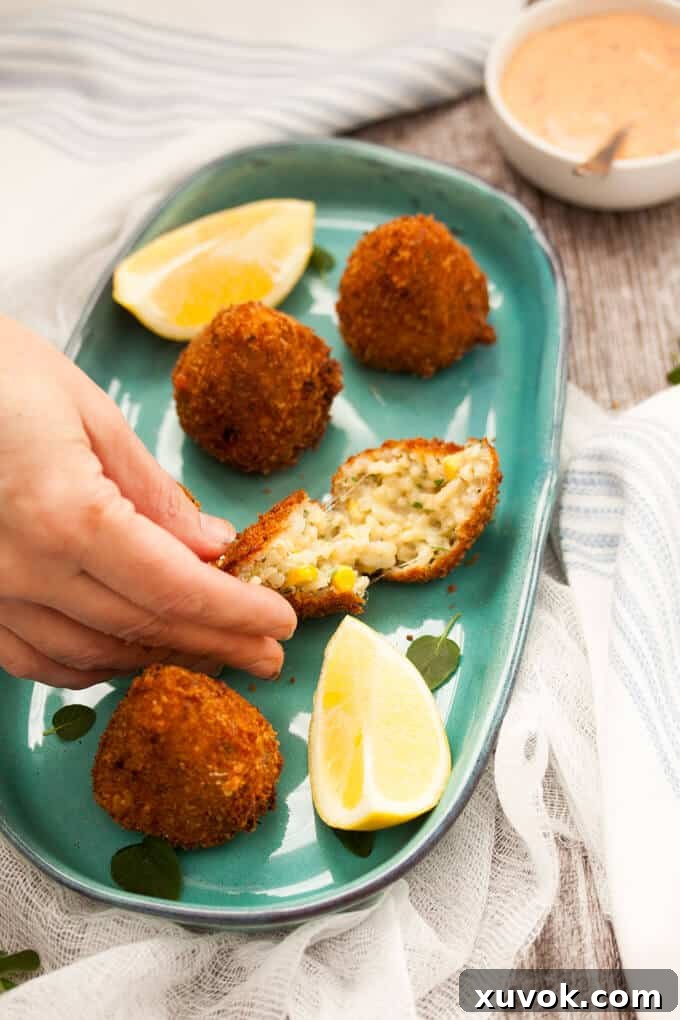 A hand reaching into the frame to gently pick up a perfectly fried vegetarian sweet corn arancini, emphasizing its irresistible appeal.