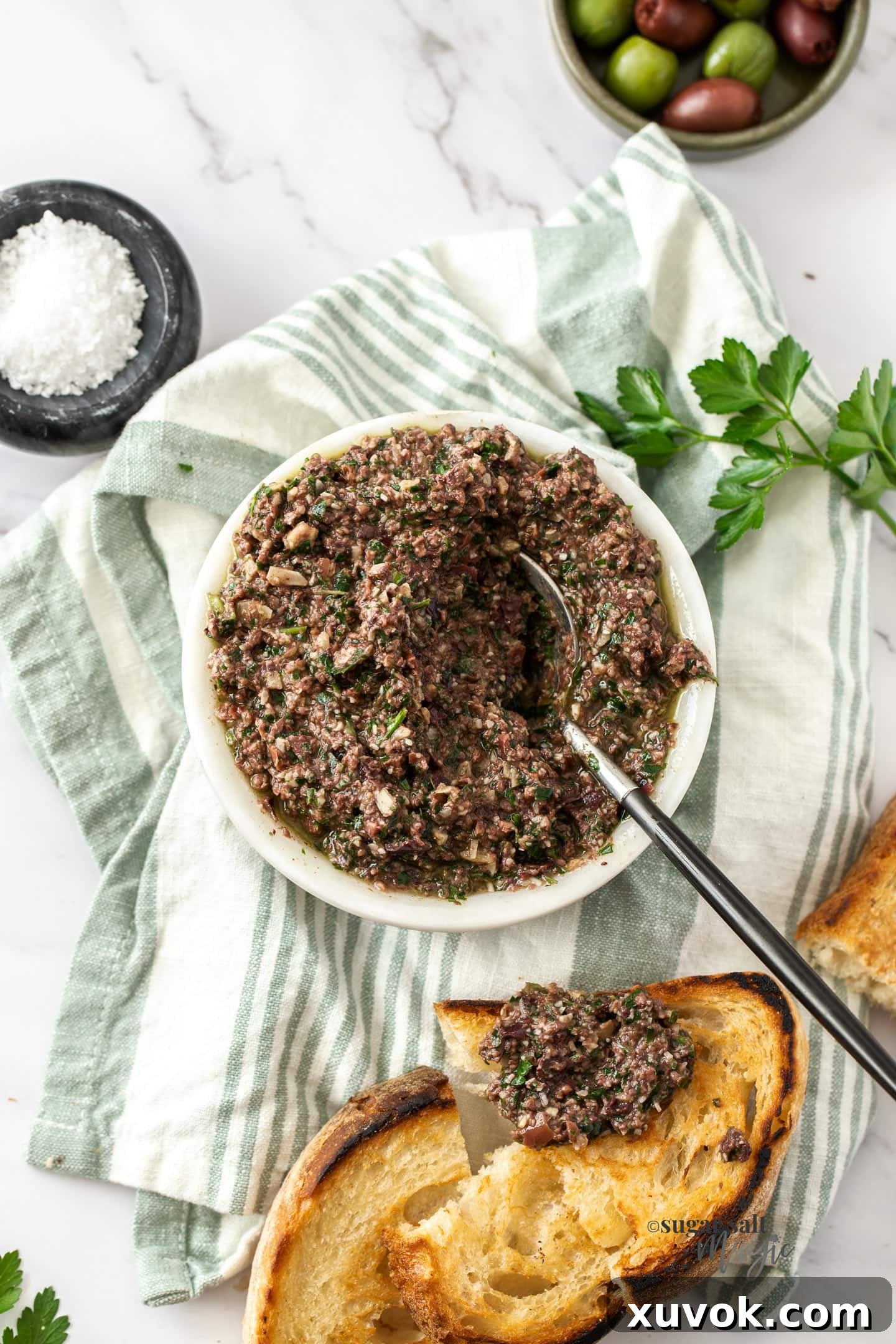 A vibrant bowl of homemade Kalamata olive pesto, surrounded by fresh olives and crispy toasted bread slices, ready to be enjoyed as a gourmet appetizer or spread.