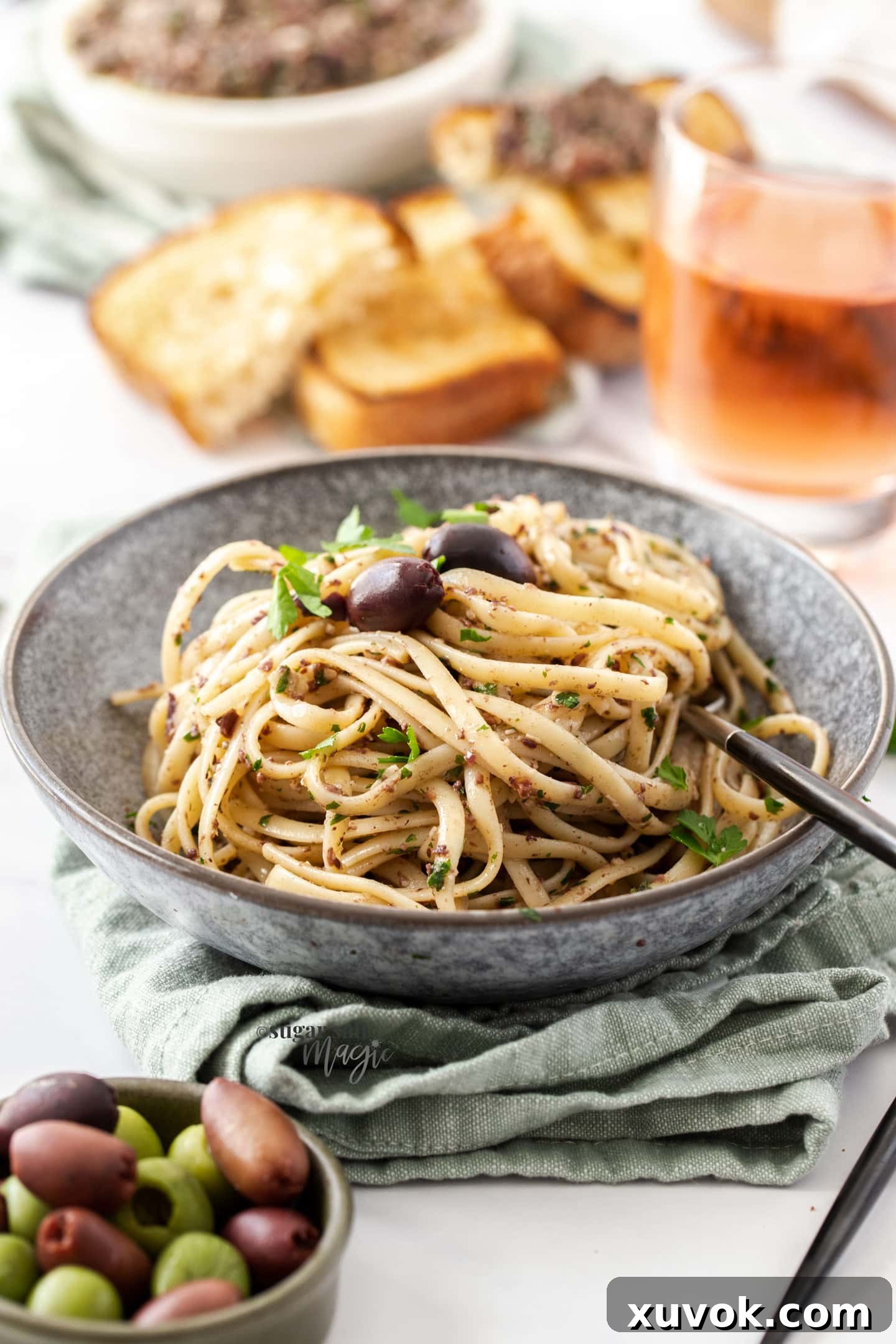 A grey bowl filled with perfectly cooked pasta tossed with olive pesto and garnished with fresh olives, showcasing a delicious meal idea.