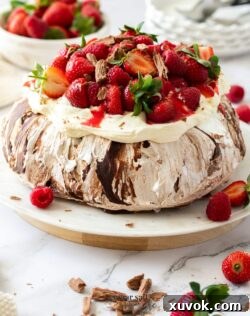 A chocolate pavlova topped with cream and berries on a white cake plate
