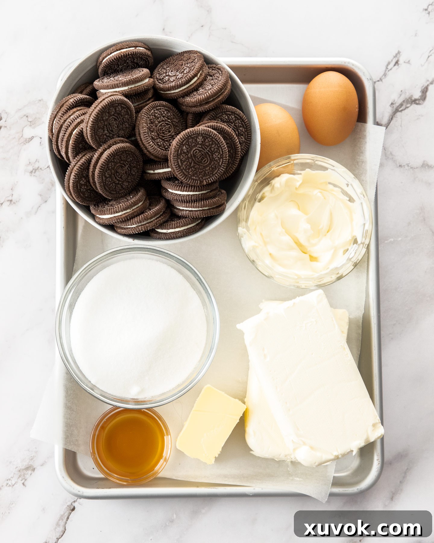 All the essential ingredients for making Oreo cheesecake bars, neatly arranged on a baking tray, including cream cheese, Oreos, butter, and eggs.