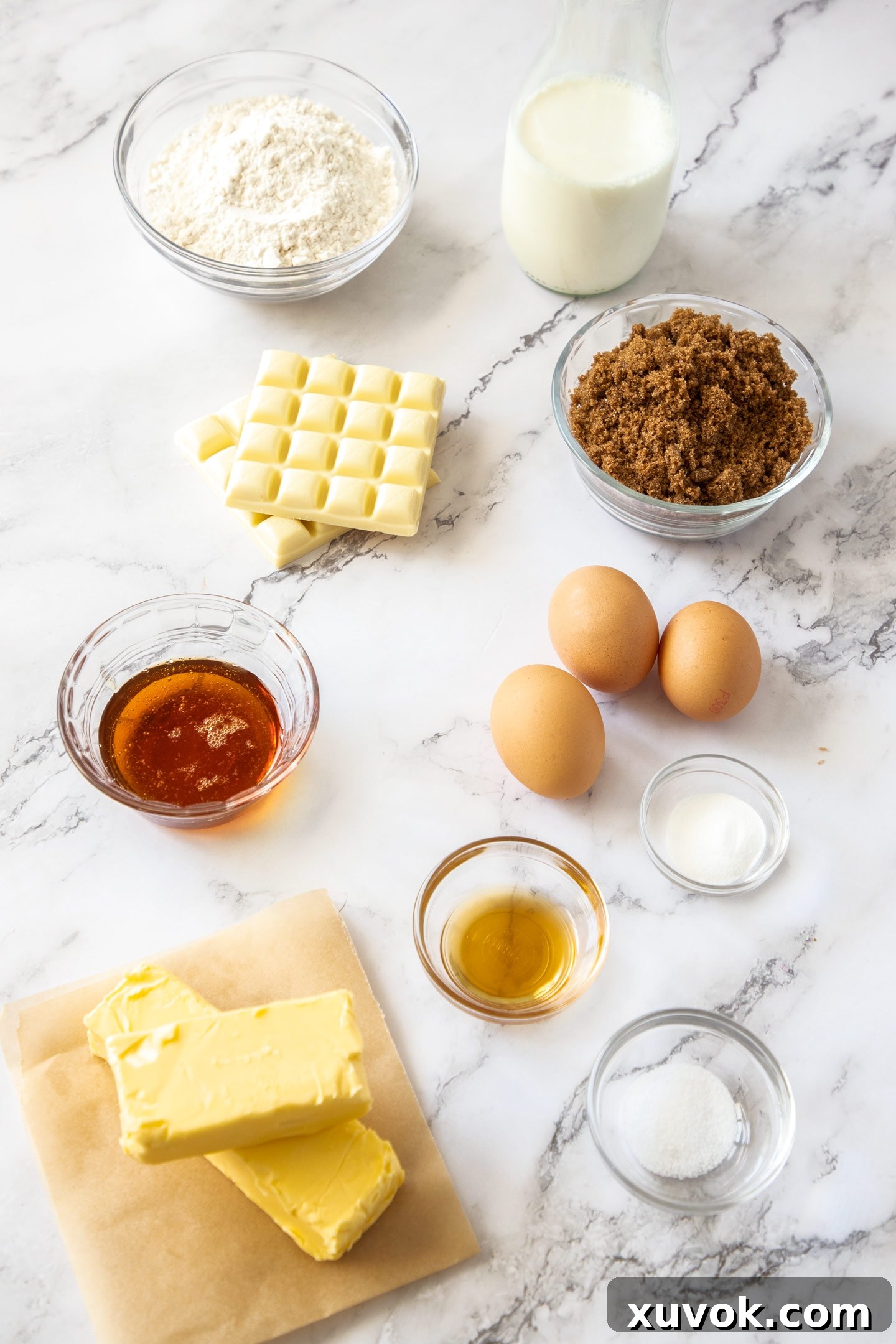 A collection of caramel mud cake ingredients laid out on a elegant marble surface, including dark brown sugar, golden syrup, white chocolate, milk, and eggs, ready for baking.