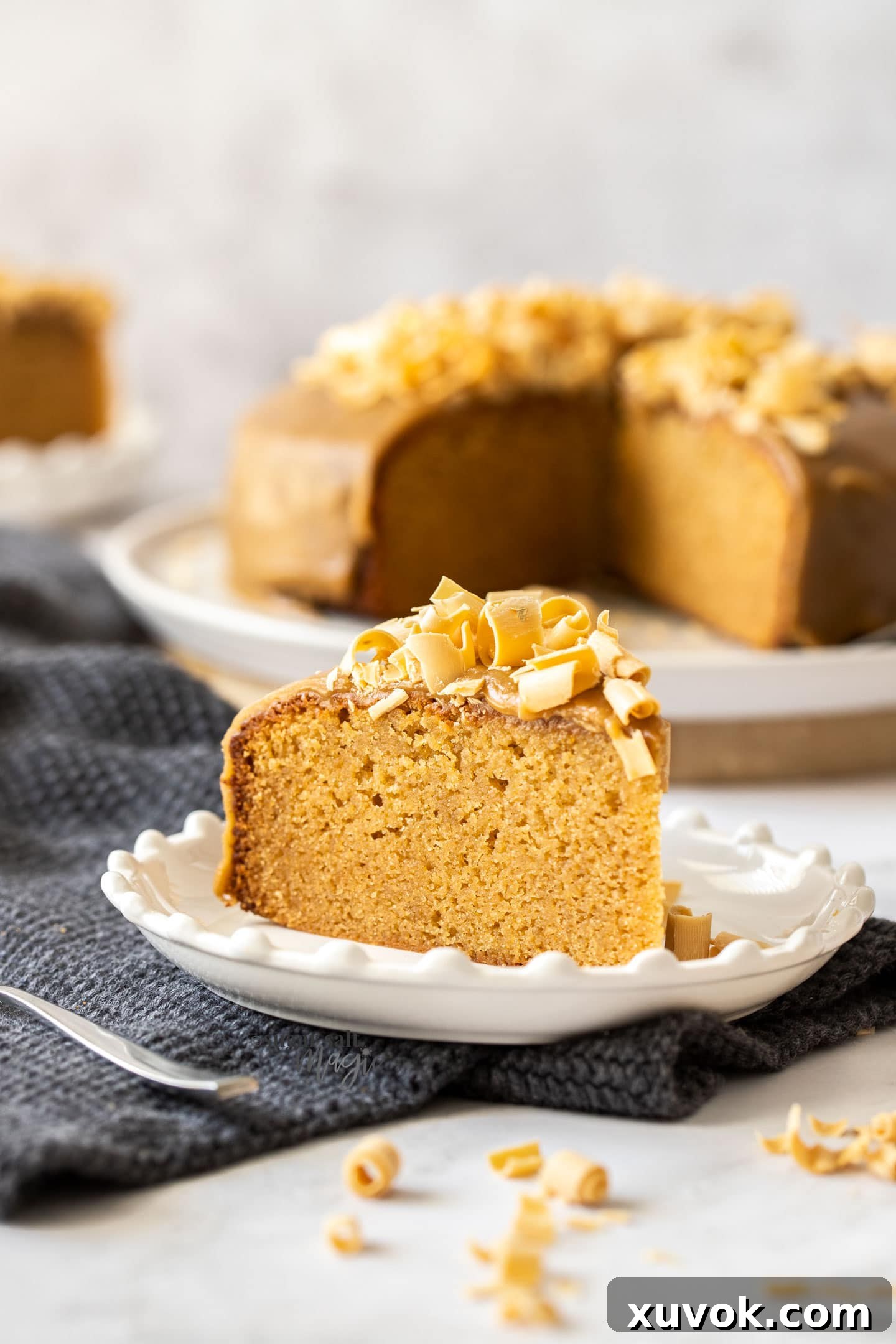 A perfectly sliced piece of caramel mud cake, revealing its dense, moist crumb, topped with delicate chocolate shavings, resting on a white plate. Ready to be enjoyed.