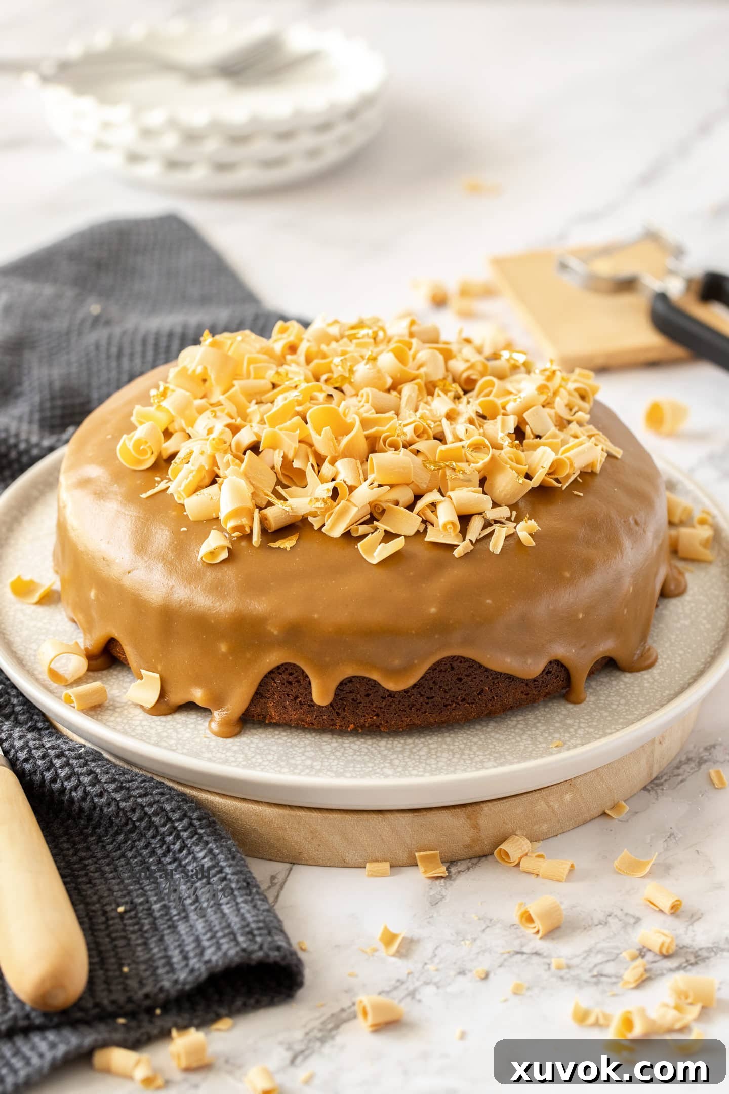 Two caramel mud cakes, one whole and one with a slice removed, adorned with white chocolate shavings, resting on a clean white backdrop. Perfect for sharing or enjoying solo.