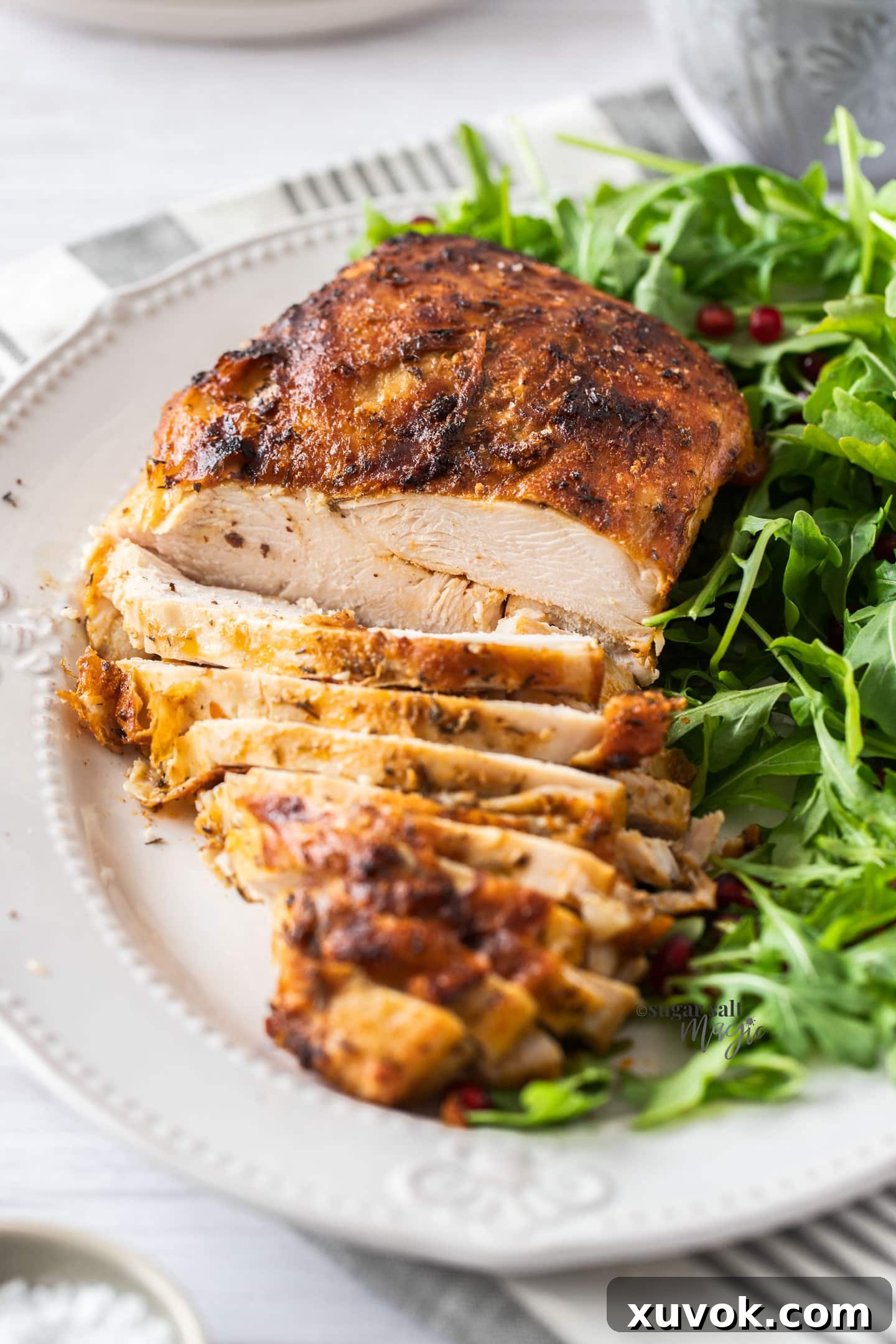 A golden turkey breast on a plate, partly sliced, with vibrant green salad on the side. The turkey boasts a perfectly crisp, golden-brown skin and moist, tender meat.