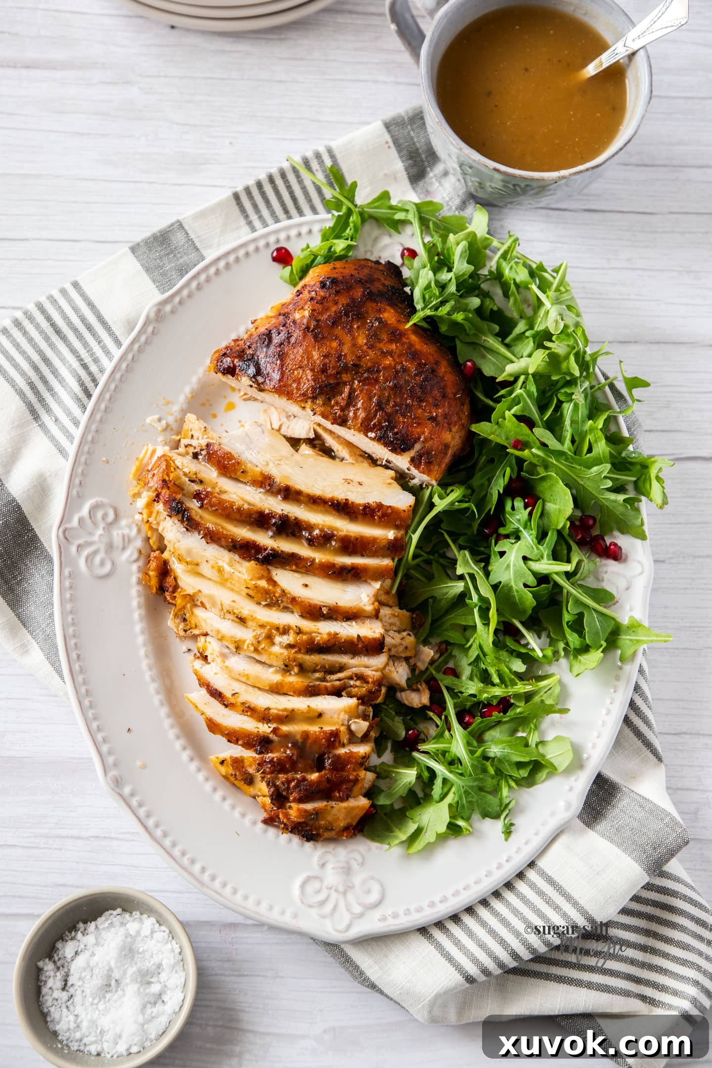 A golden-brown, perfectly cooked turkey breast on a white plate, partially sliced to reveal its juicy interior, accompanied by a fresh green salad. The skin is visibly crisp and inviting.