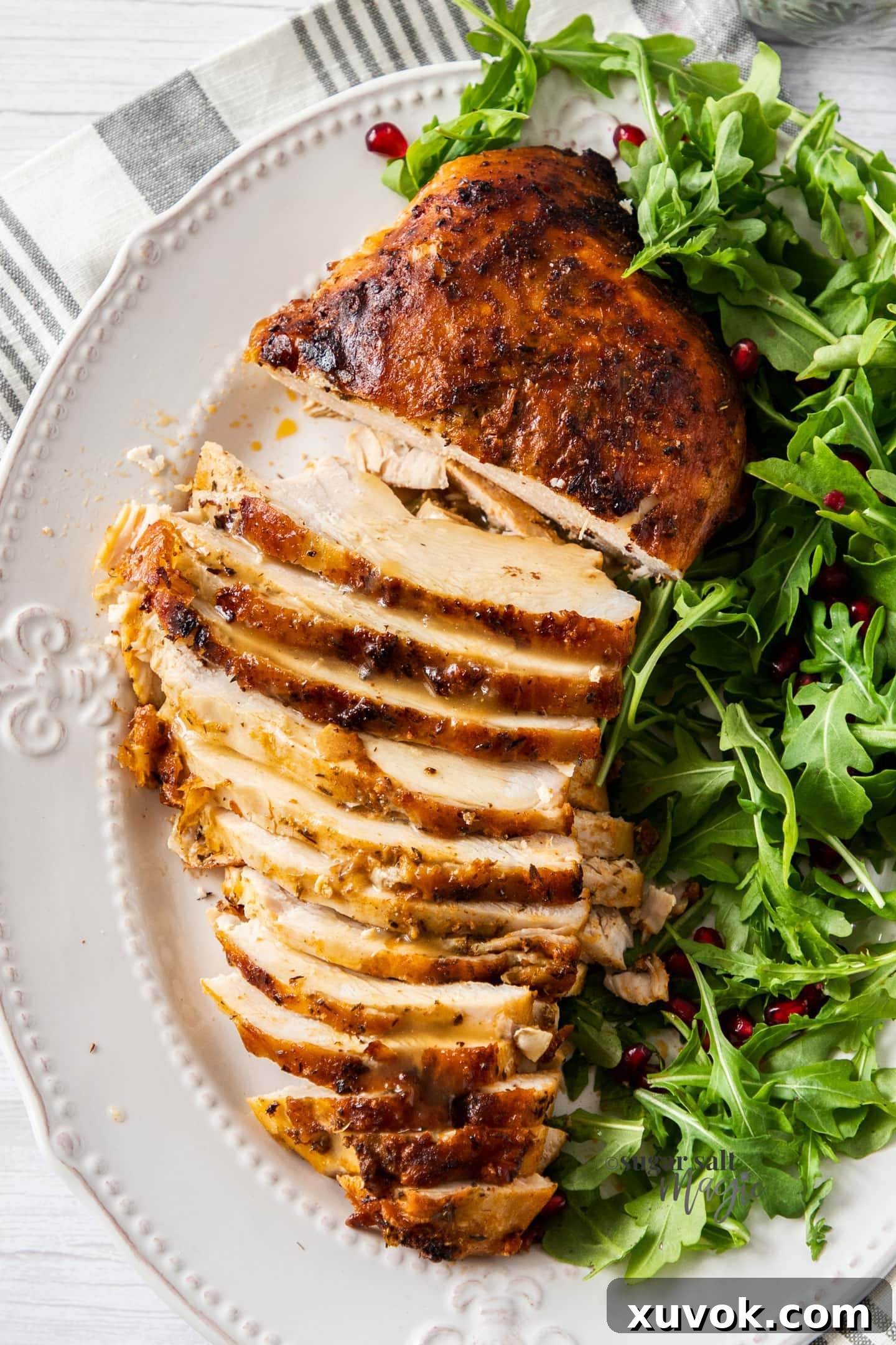 A beautifully presented golden turkey breast on a plate, partially sliced to showcase its tender texture, served alongside a fresh and vibrant green salad.
