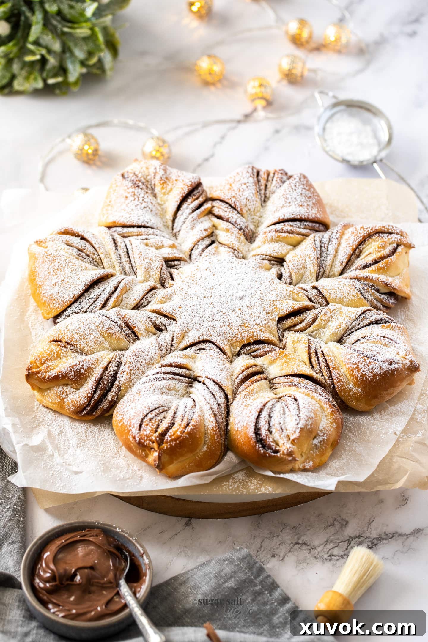 A star shaped bread on a sheet of baking paper with a grey tea towel nearby, emphasizing its pull-apart layers
