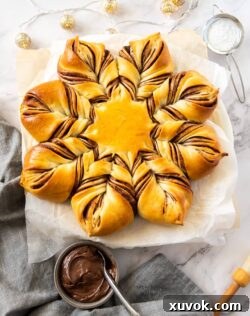 A star shaped bread on a sheet of baking paper with a grey tea towel nearby