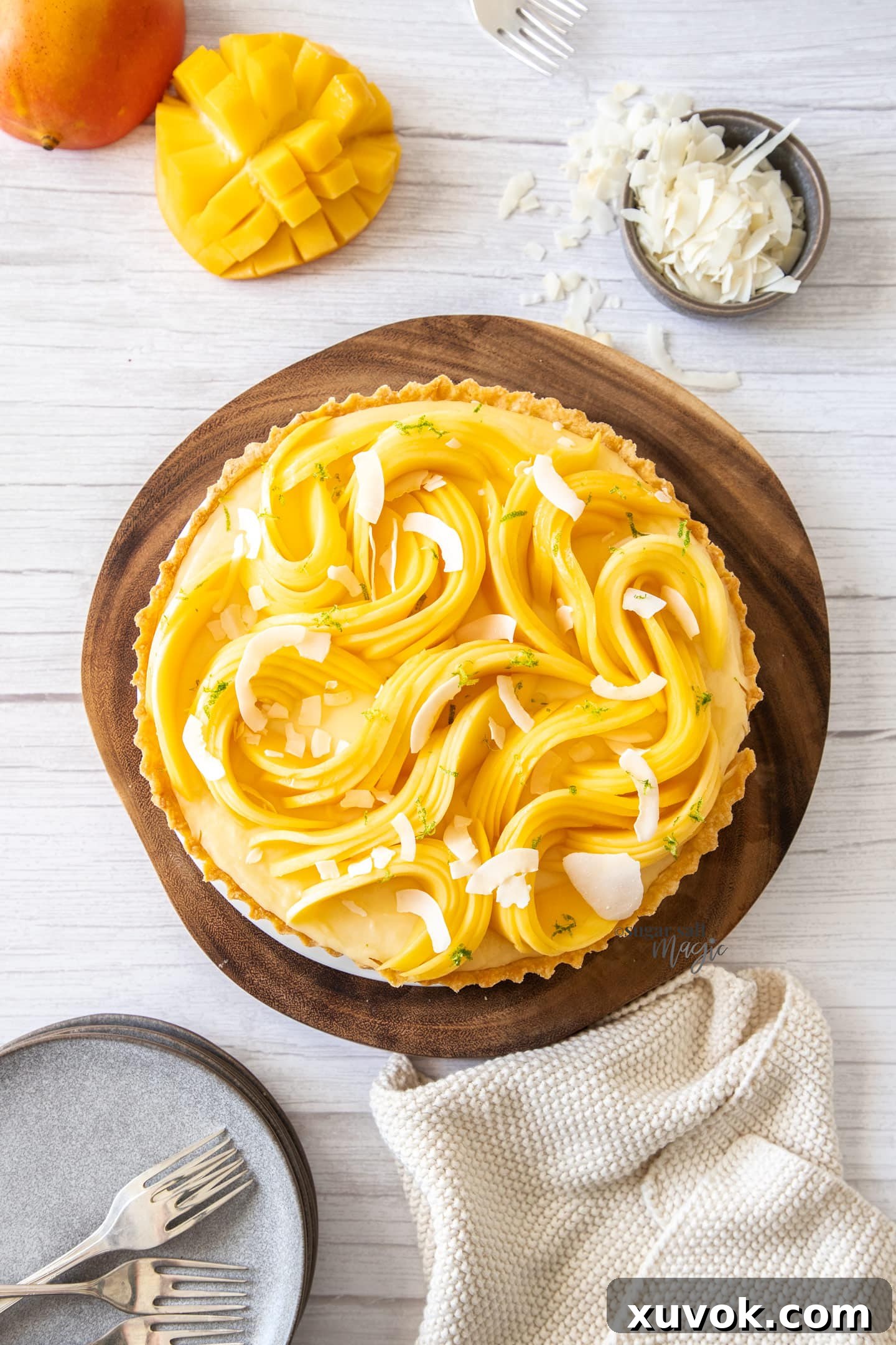 Top down view of a tart covered in sliced mango sitting on a wooden board.