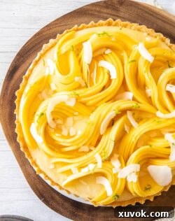 Top down view of a tart covered in sliced mango sitting on a wooden board