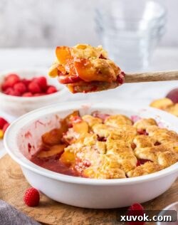 A spoonful of raspberry peach cobbler being lifted from a pie dish full of the delicious dessert.