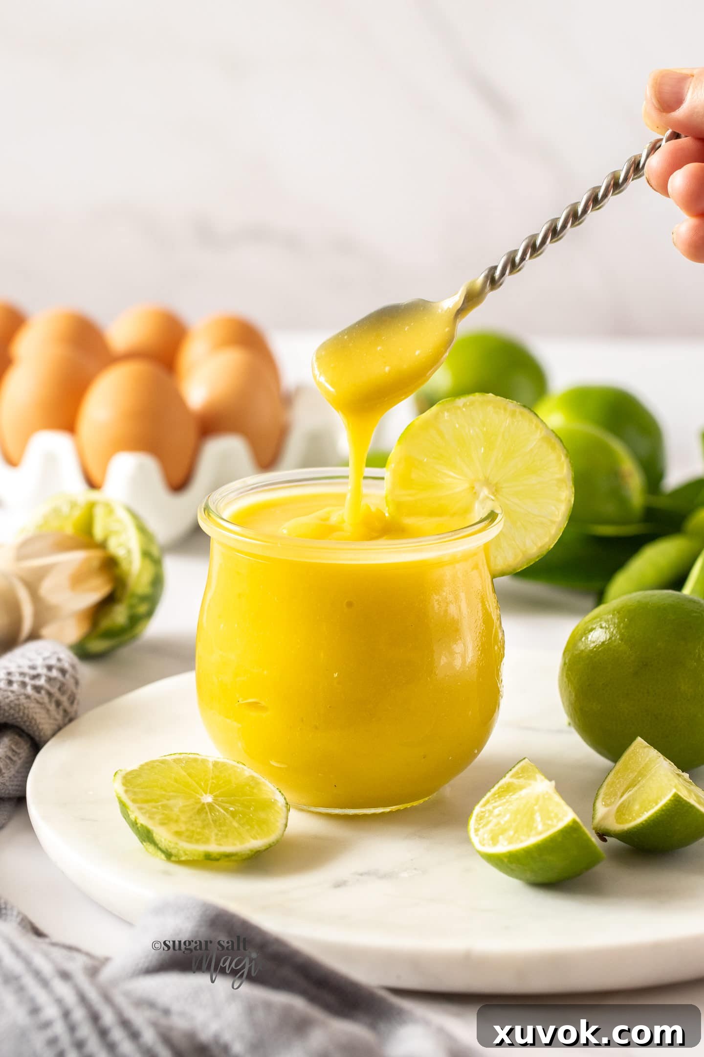 A spoon hovering over a glass jar filled with luscious homemade lime curd, highlighting its vibrant color and smooth texture.