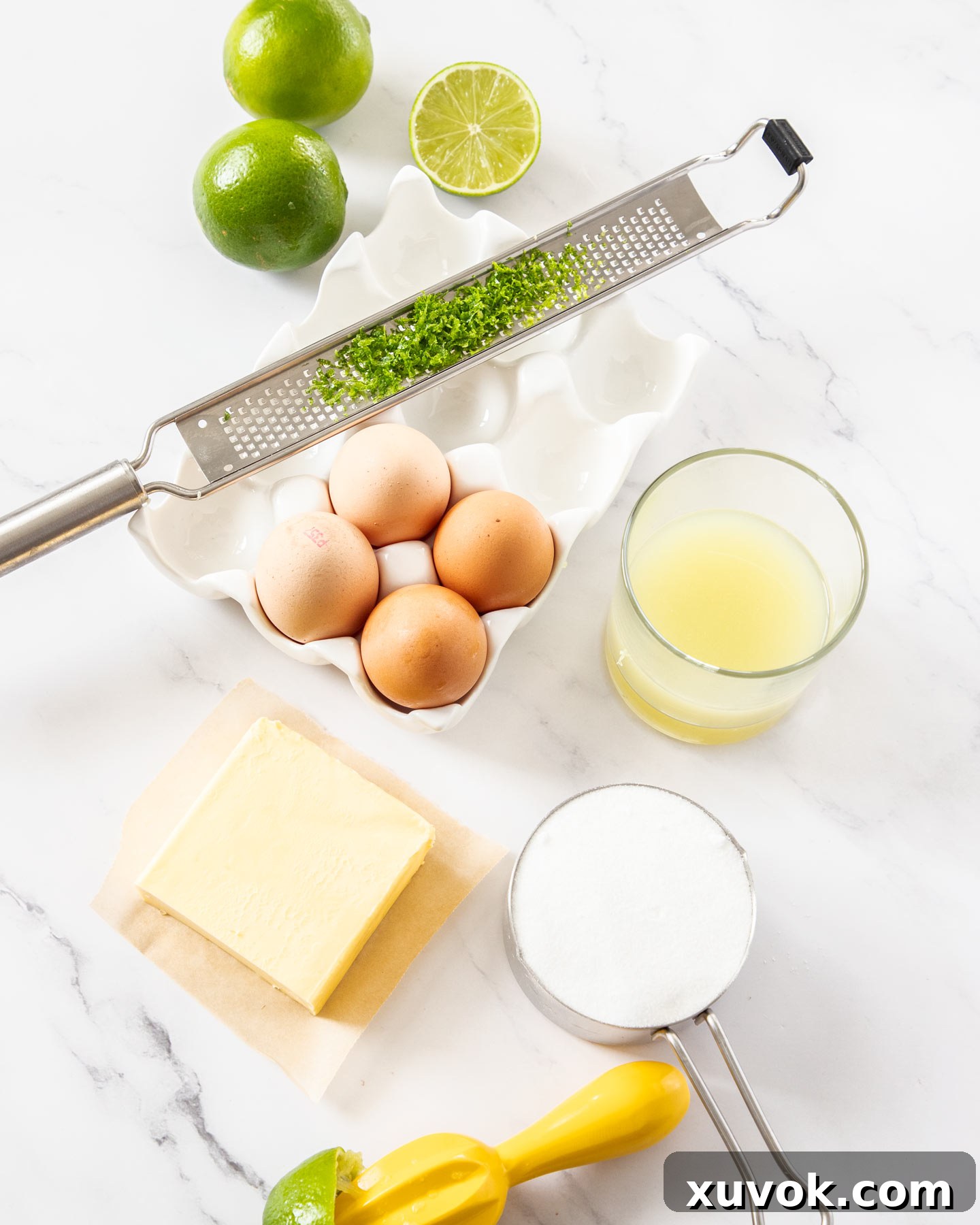 A selection of fresh ingredients laid out for making lime curd, including limes, eggs, butter, and sugar.
