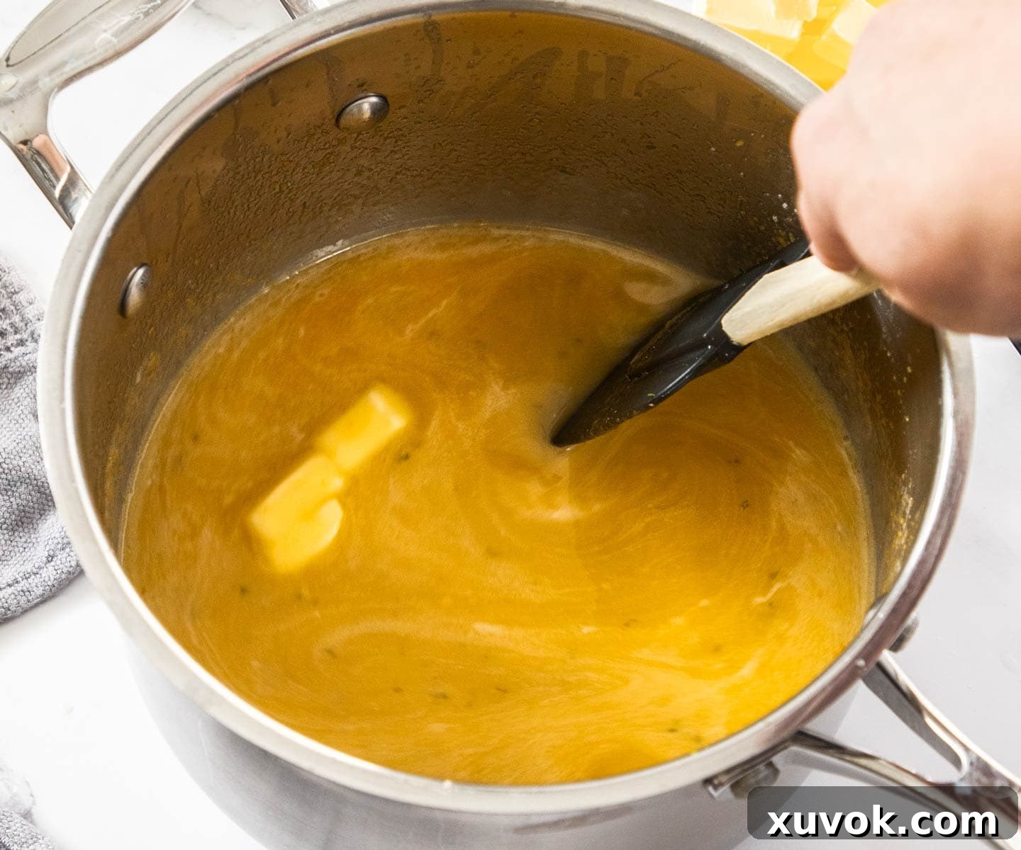 Small cubes of butter being stirred into the lime curd mixture in a saucepan, melting and enriching the flavor.