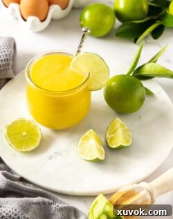 A glass jar filled with luscious lime curd on a white platter, surrounded by fresh limes and eggs, ready for serving.
