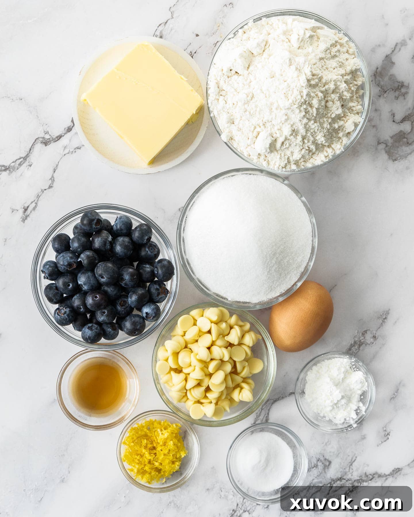 Fresh ingredients for blueberry and white chocolate cookies laid out on a marble surface.