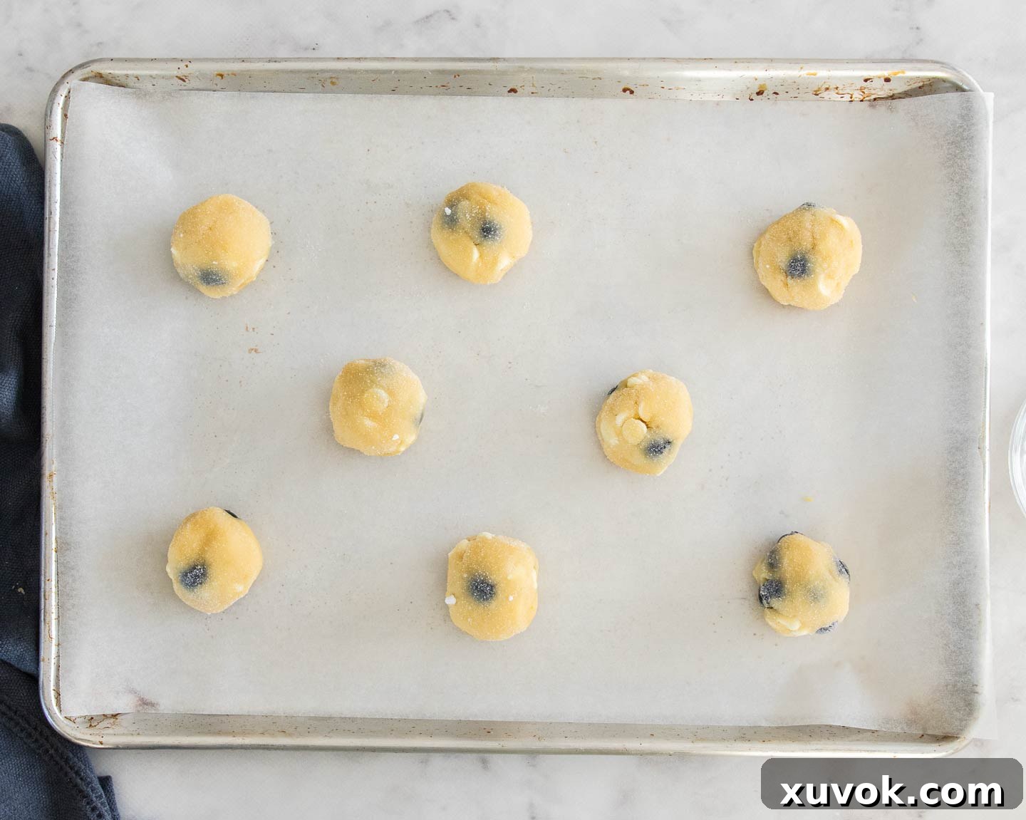 Balls of blueberry white chocolate cookie dough on a baking sheet, ready for baking.