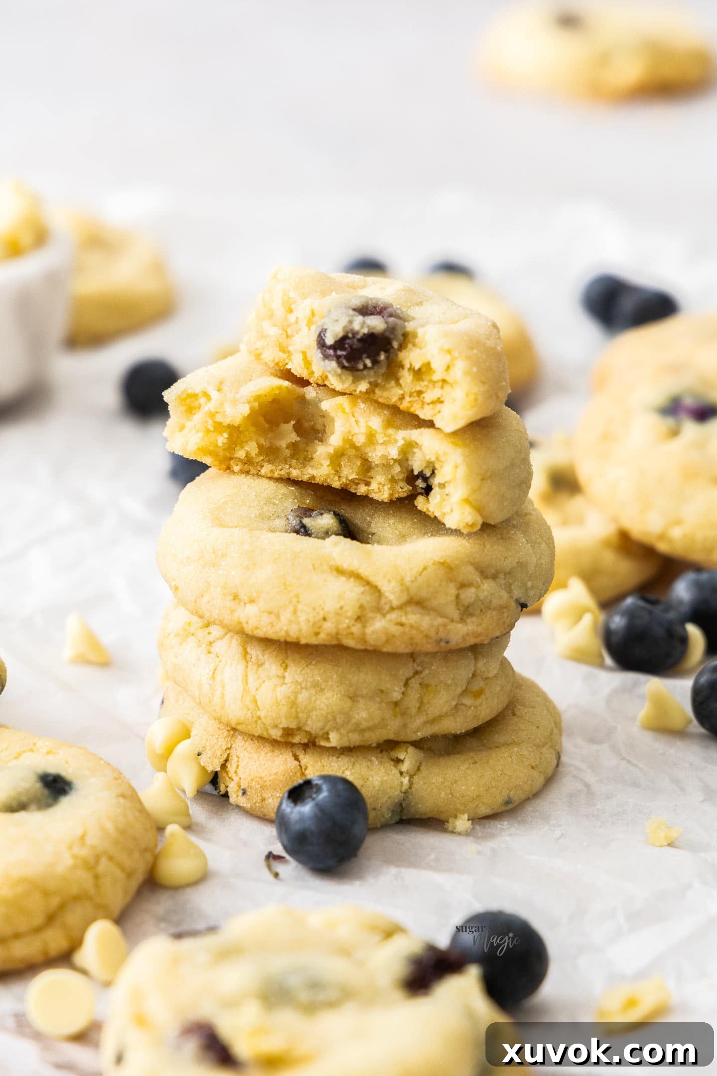 A beautiful stack of blueberry white chocolate cookies with the top cookie broken in half, revealing the soft interior and berries.