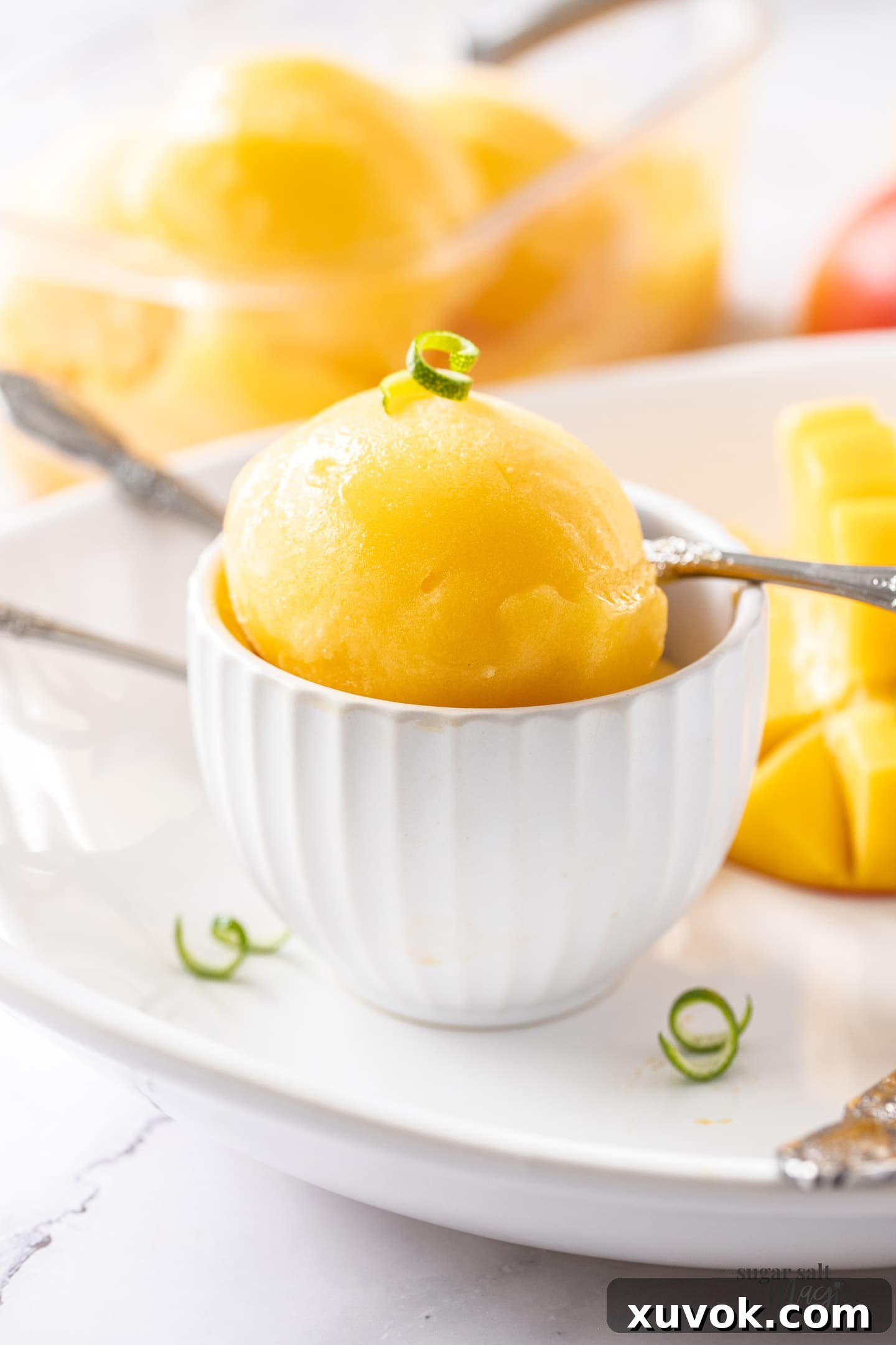 A white bowl showcasing a generous scoop of vibrant, smooth mango sorbet, garnished lightly.