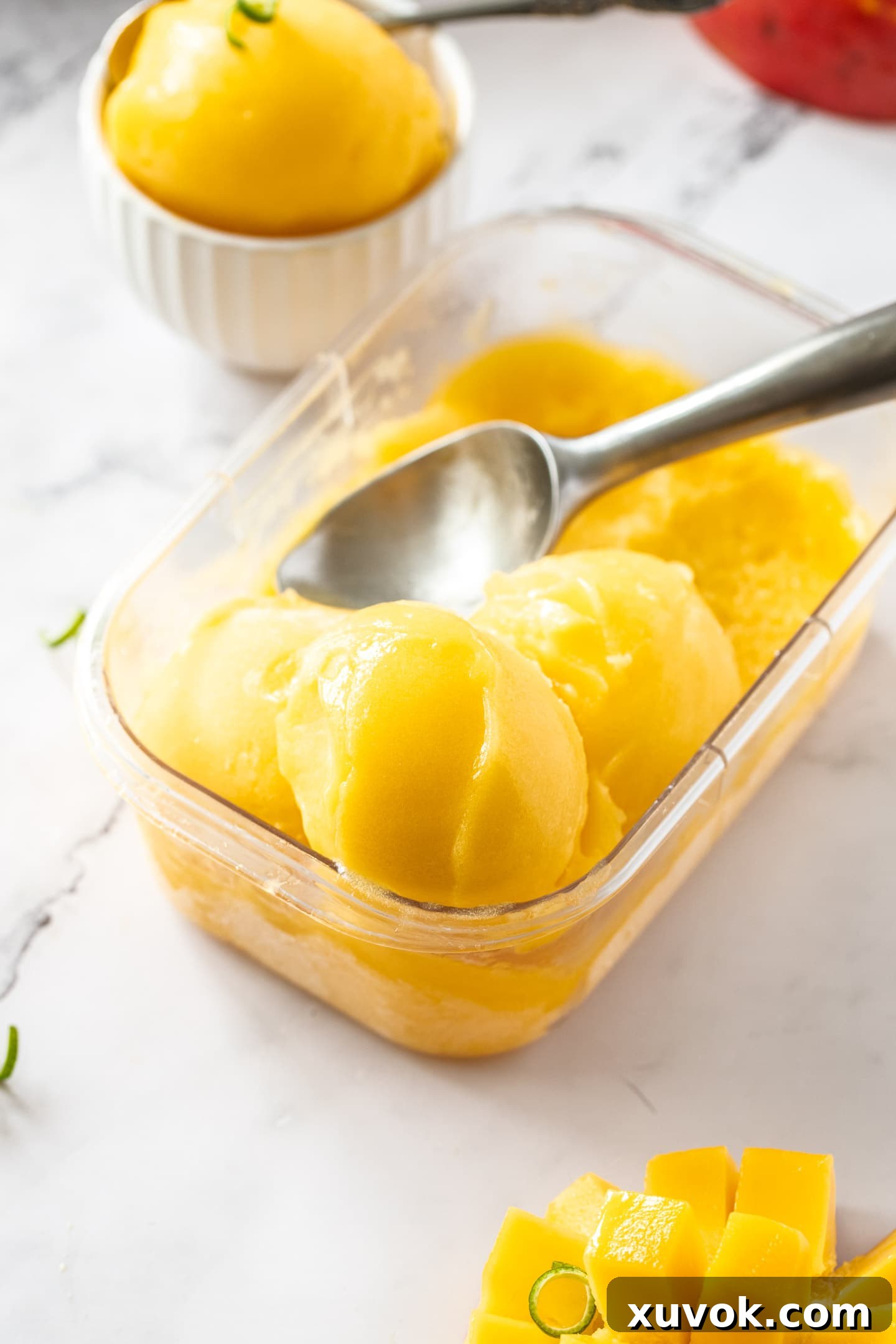 A clear, freezer-safe container filled with beautifully scooped portions of golden mango sorbet, ready for enjoyment.