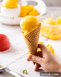 A waffle cone holds a perfect scoop of vibrant mango sorbet, highlighting its smooth and appealing texture.
