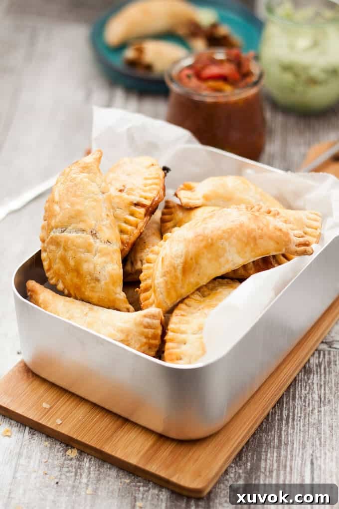 A close-up shot of several baked pulled pork empanadas in a rustic metal tray, highlighting their golden, textured crusts and inviting appearance.